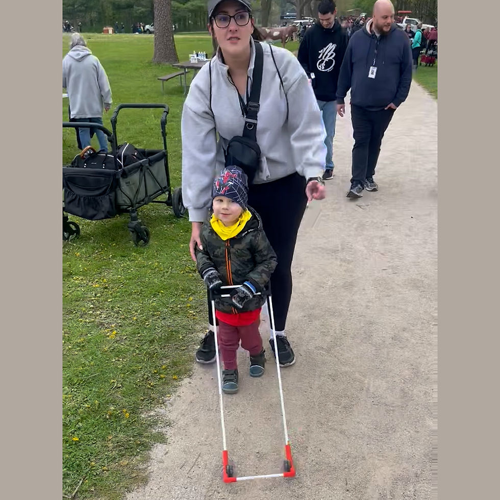 Woman and child wearing a Belt Cane on a park path. The woman wears a cap and crossbody bag, the child a winter hat. Green grass nearby.