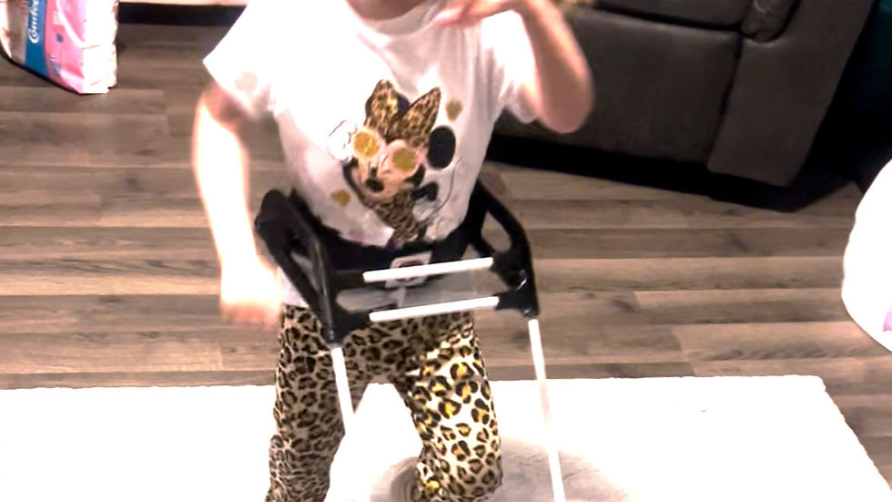 4-year-old girl wearing a belt cane walks across the carpet in her home with a smile on her face, right hand in the air, left arm by her side, right knee bent and foot off the ground, ponytail waving far to the right side.