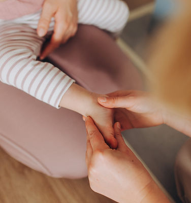 Kind sitzt auf Schoß von Mama, Kinderfuß wird therapeutisch behandelt
