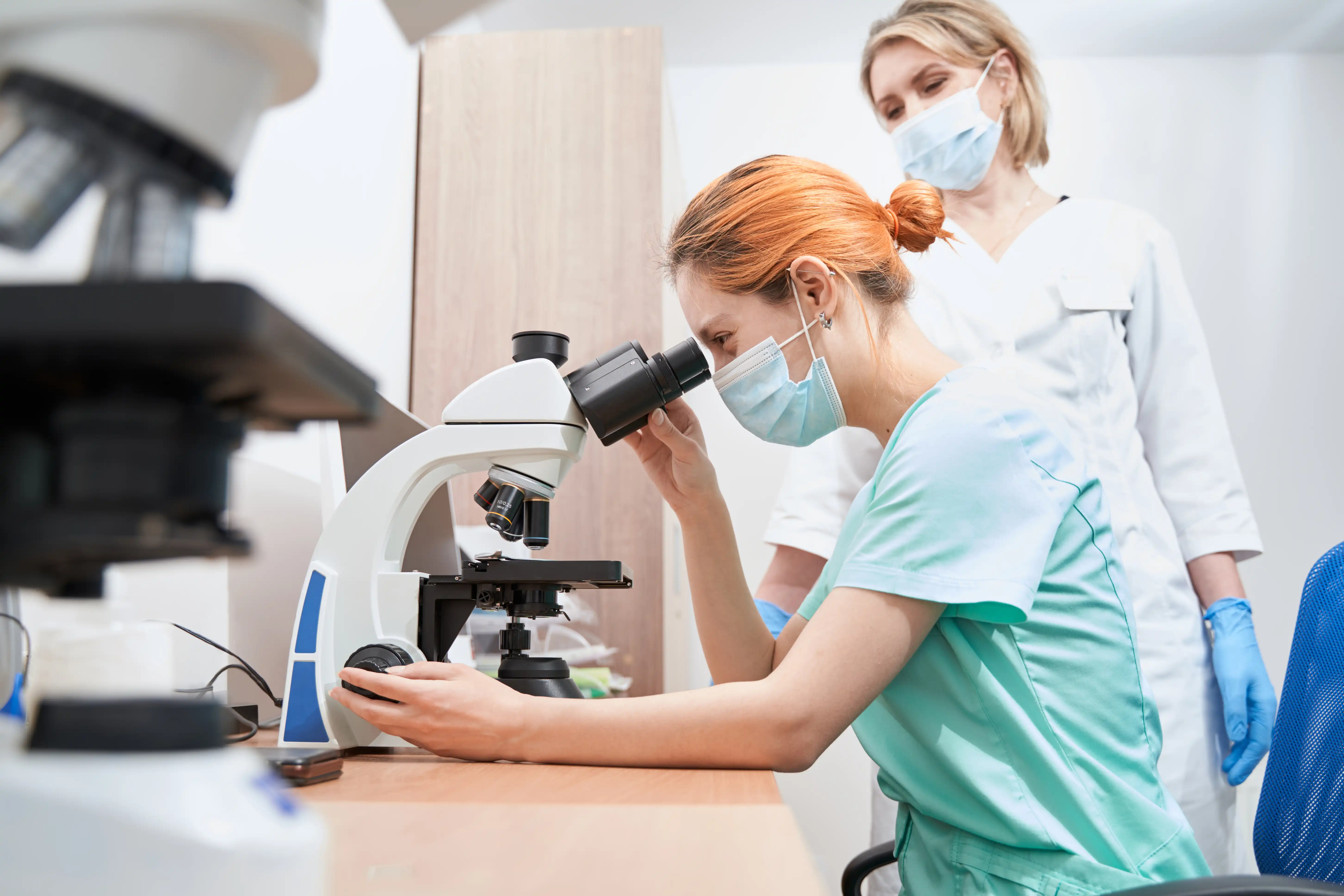 Woman wearing lab equipment looking down a microscope