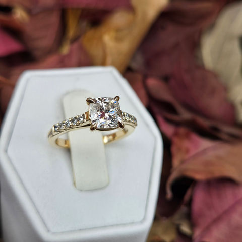 Round diamond engagement ring with a yellow gold band and diamond accents along the shoulders.