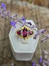 Sterling silver three-stone ring featuring a marquise-cut rhodolite garnet with trillion-cut rhodolite garnet side stones and 24K gold inlay.