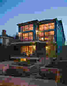 Outside of three story very modern wooden house at dusk, with the lights on in all the rooms