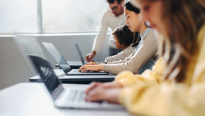 Students using Chromebooks in a 1:1 classroom while a teacher provides guidance.