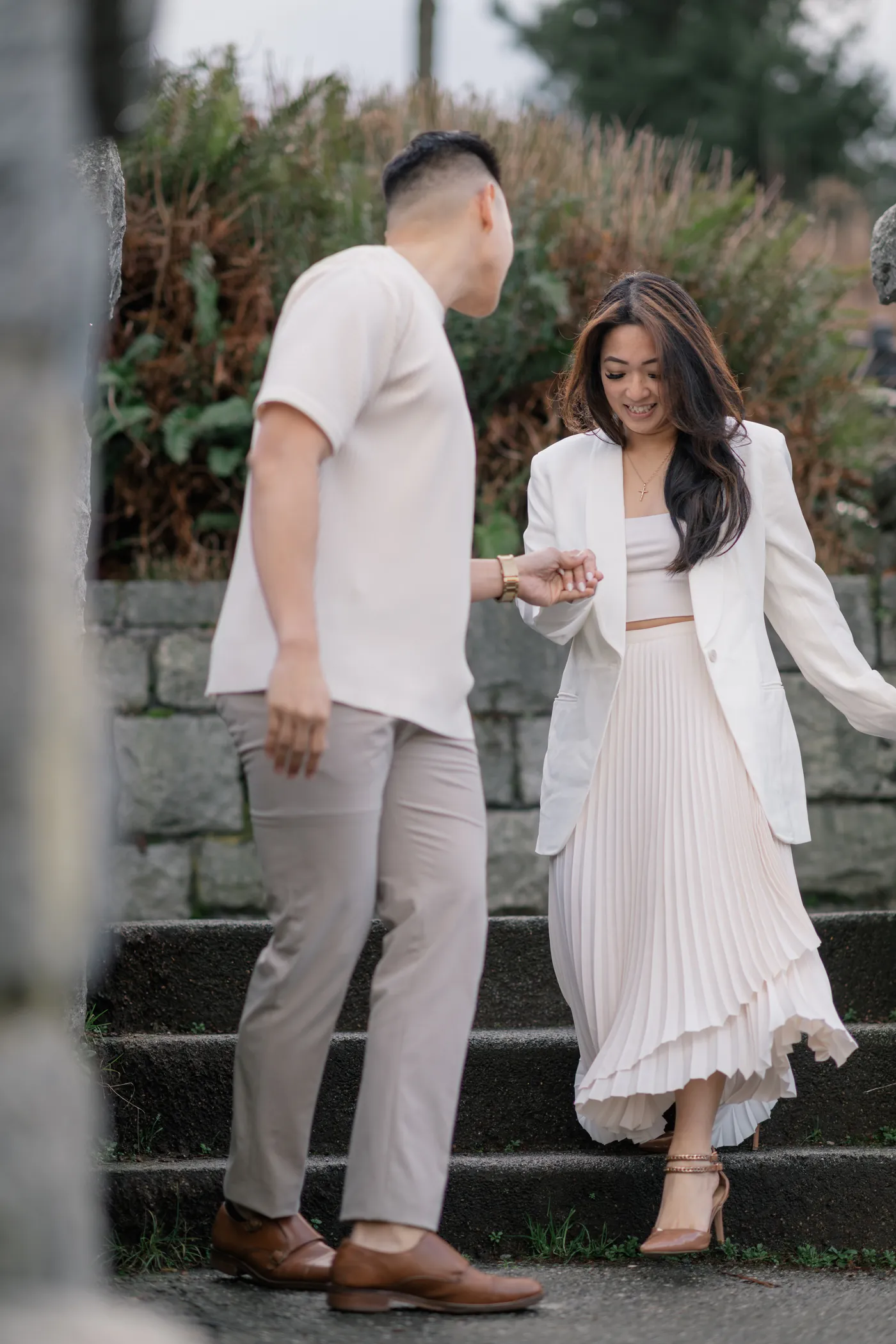 A couple walks down a stone staircase, hand in hand, during their engagement session at Stanley Park.