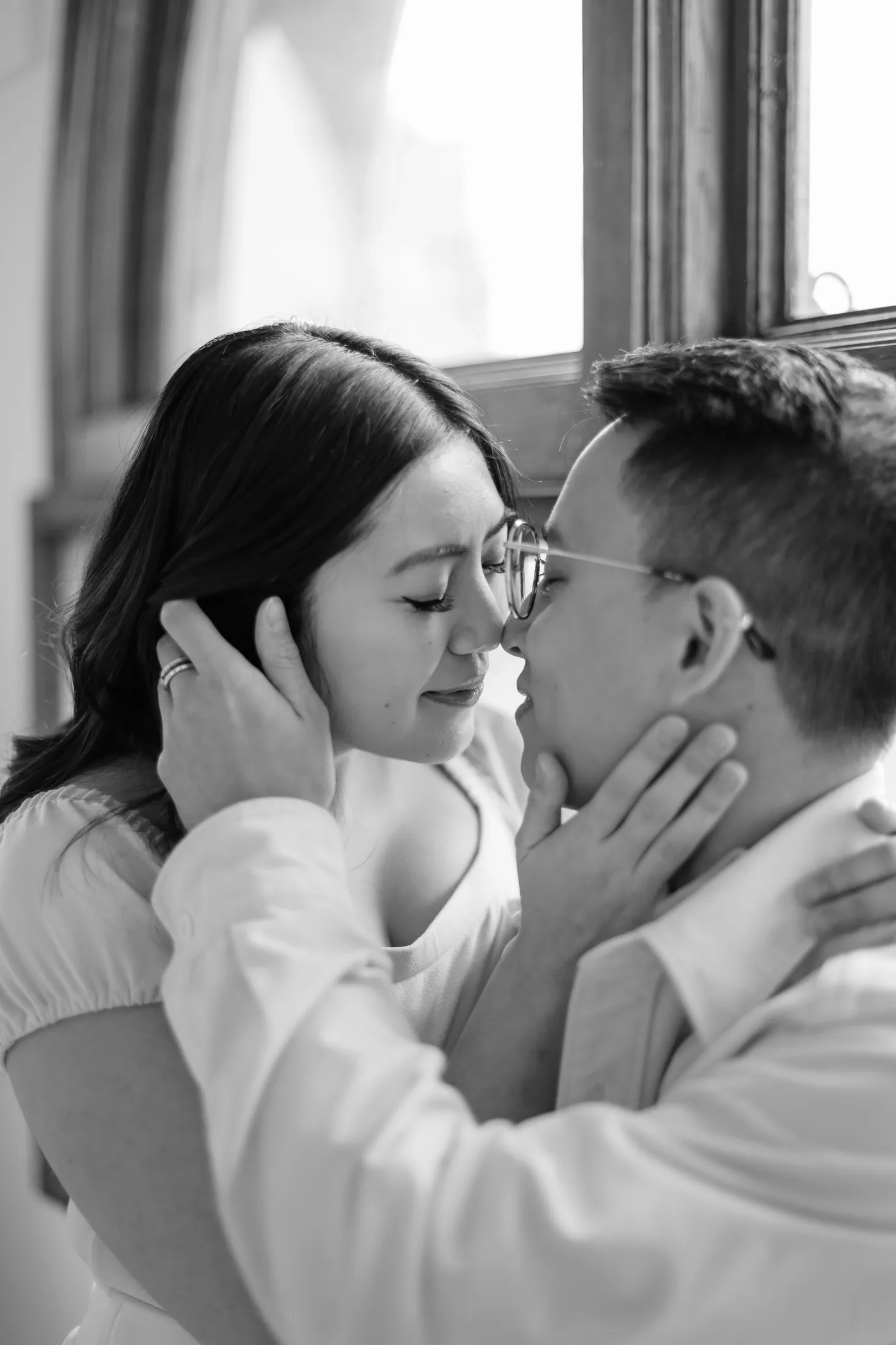 Vancouver engagement photoshoot in The Covet Studio featuring a cozy embrace with elegant arched windows in the background.