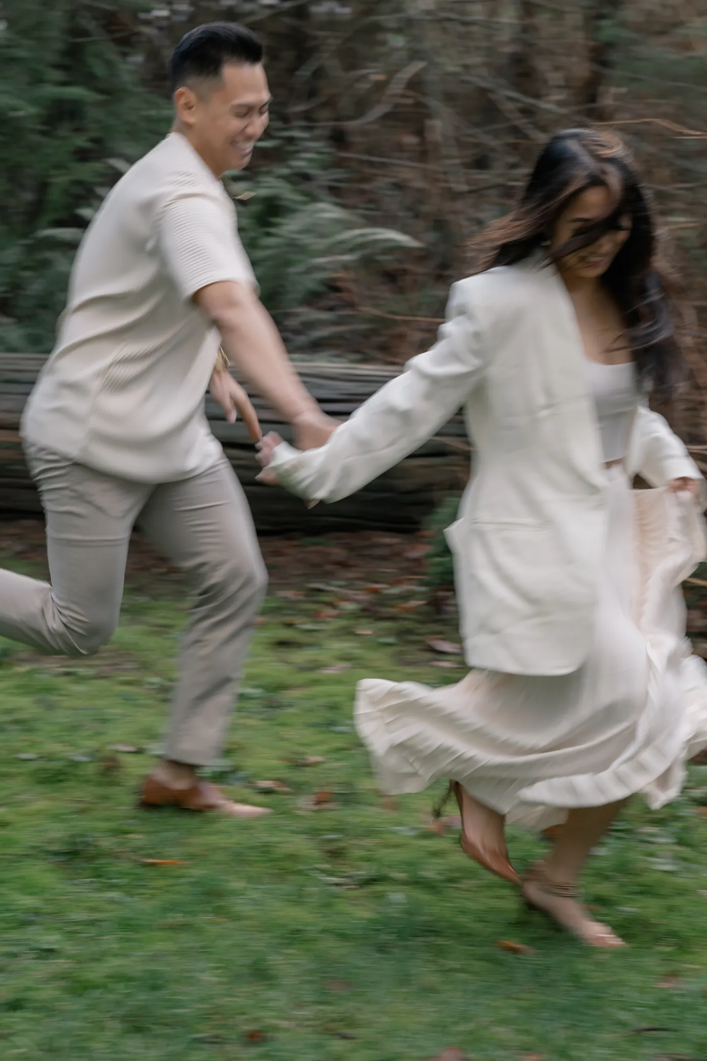 A couple running hand in hand through the greenery of Stanley Park, capturing a fun and candid engagement moment.