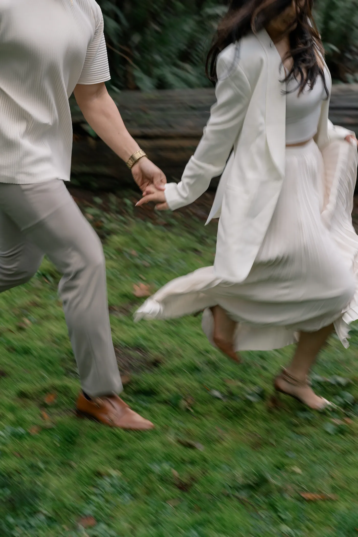 A dynamic shot of an engaged couple running through the grass at their Stanley Park engagement shoot.