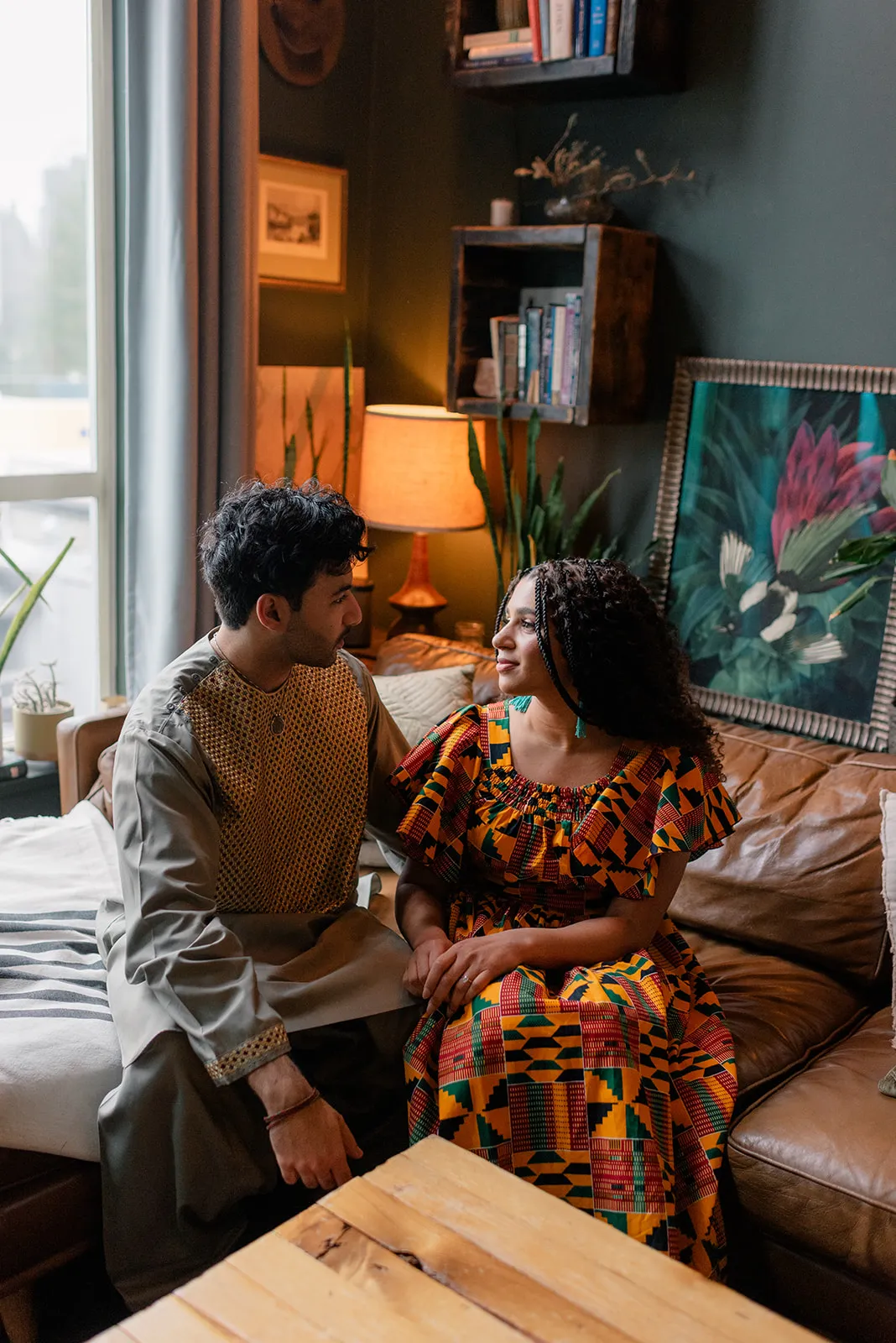 C&J posing in vibrant cultural outfits during their engagement session at Loft Garden Oasis, with a backdrop of plants and natural light