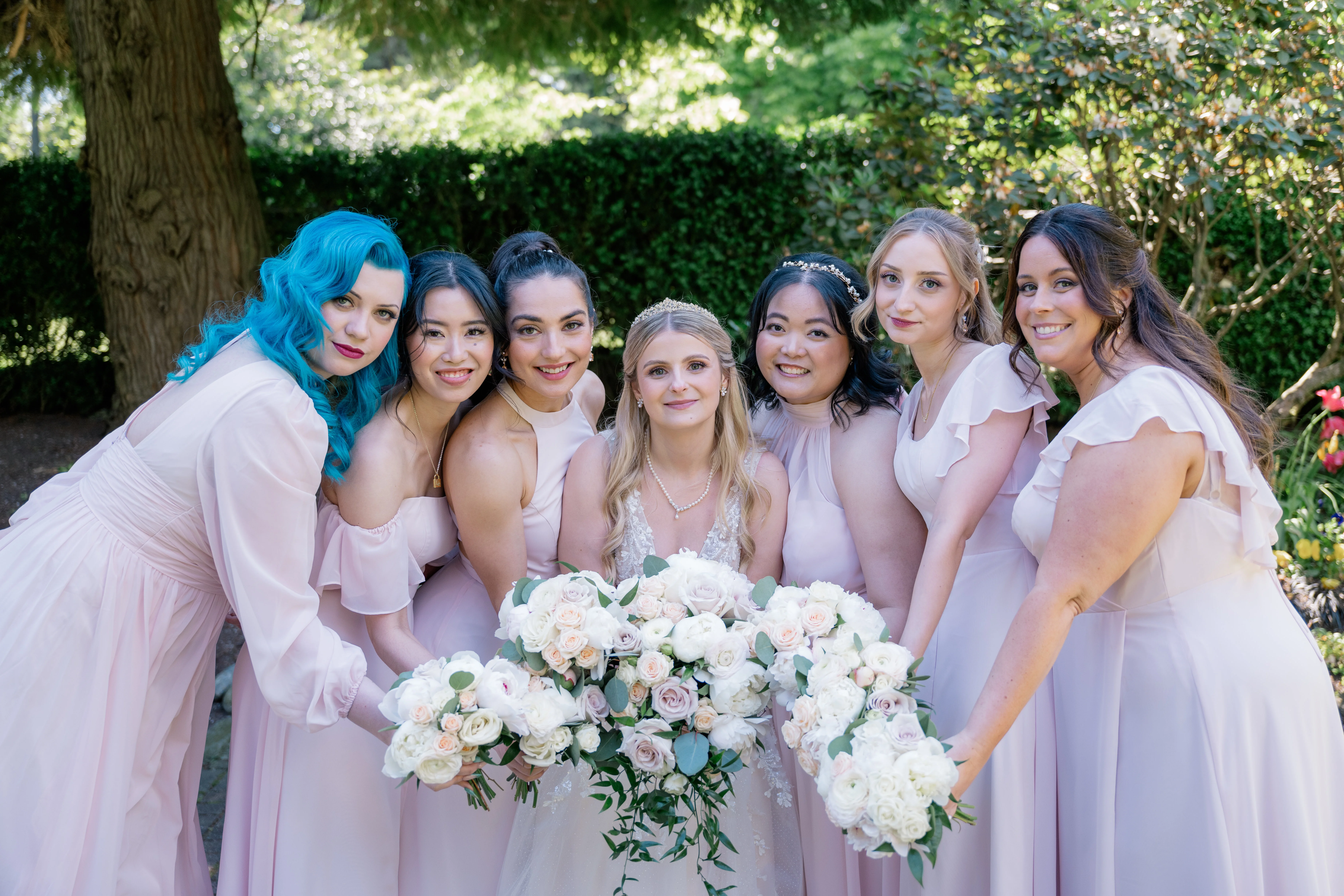 Bride laughing with her six bridesmaids in coordinating dresses, showcasing the strong bond and camaraderie among friends