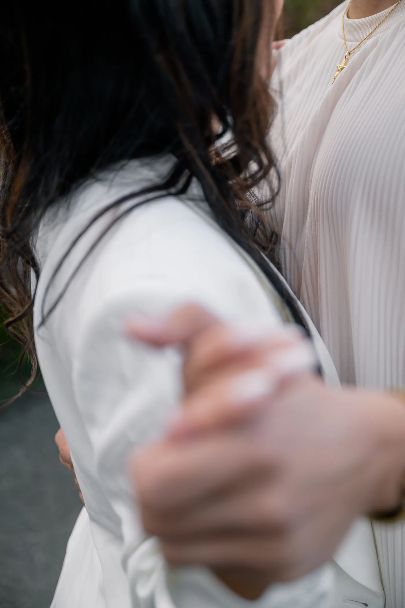A close-up of a couple’s hands intertwined, highlighting their elegant attire and engagement rings