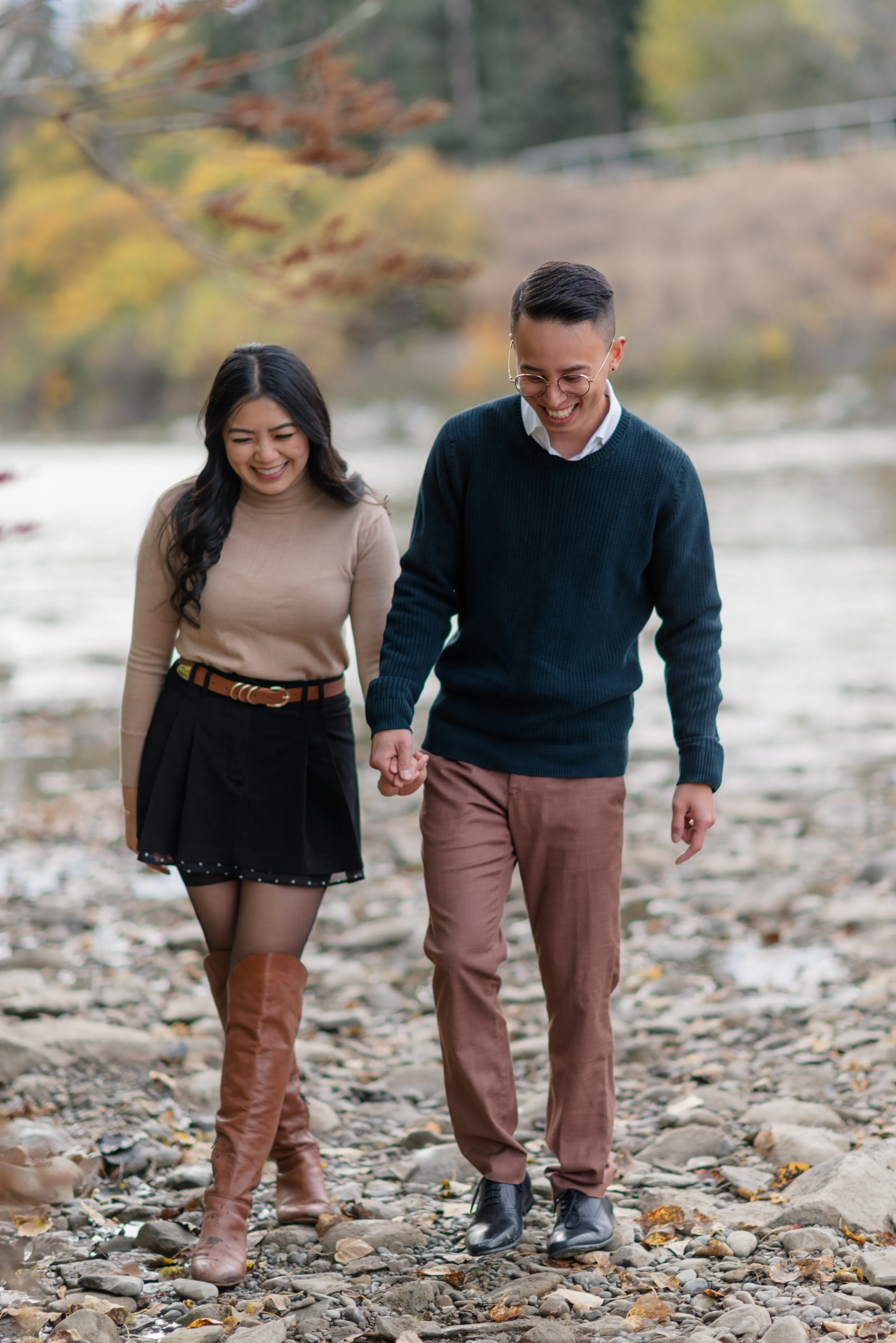 Candid engagement portrait of couple walking through shallow river rocks