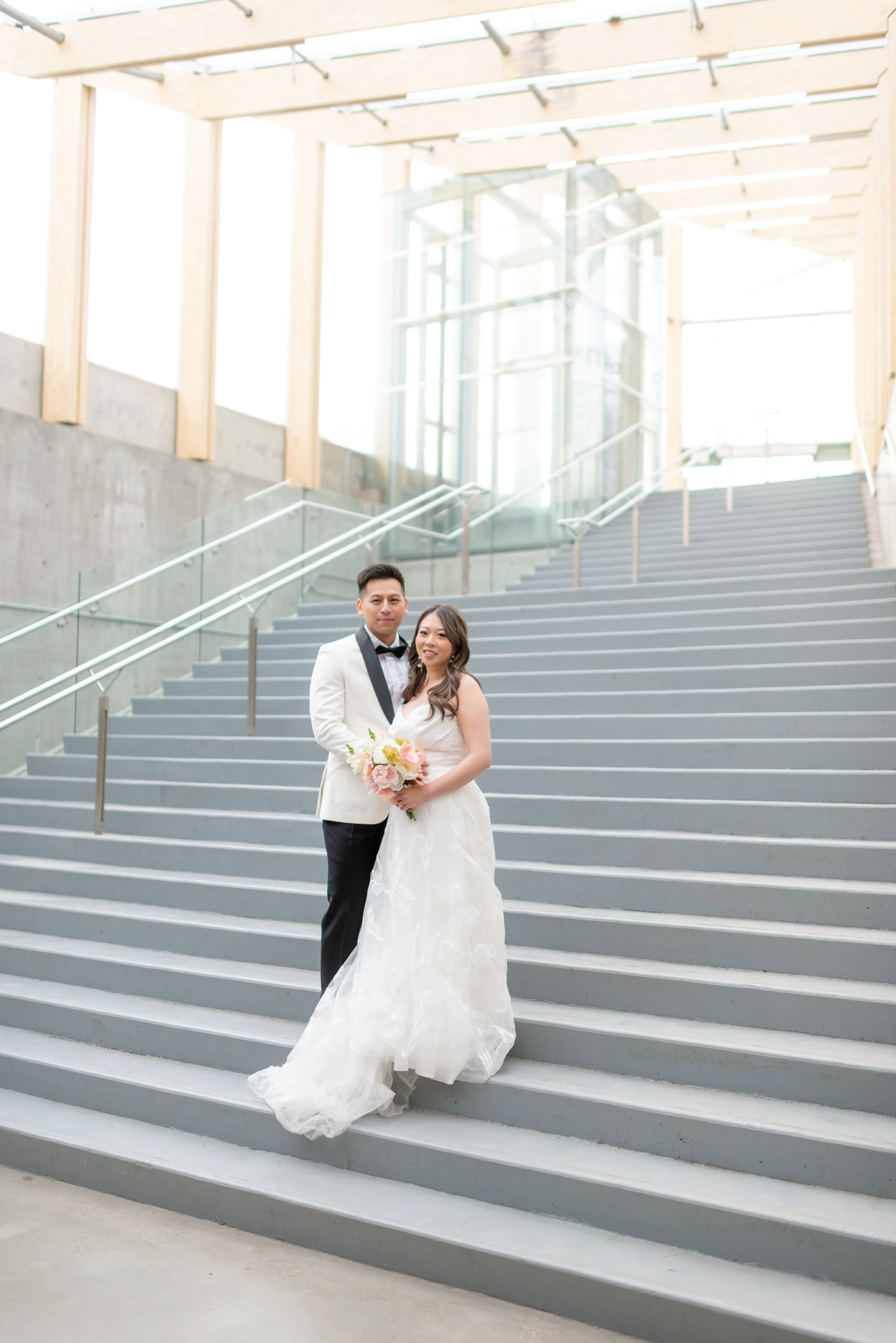 Groom holding bride close inside SAIT Polytechnic Parkade with natural window light