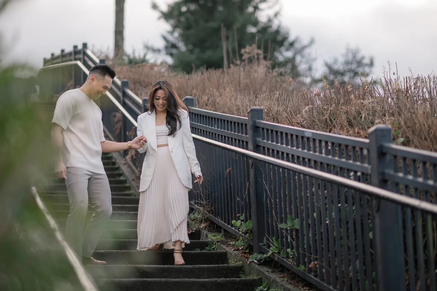 A couple walks down a scenic staircase with a fence-lined path, capturing a romantic moment at Stanley Park