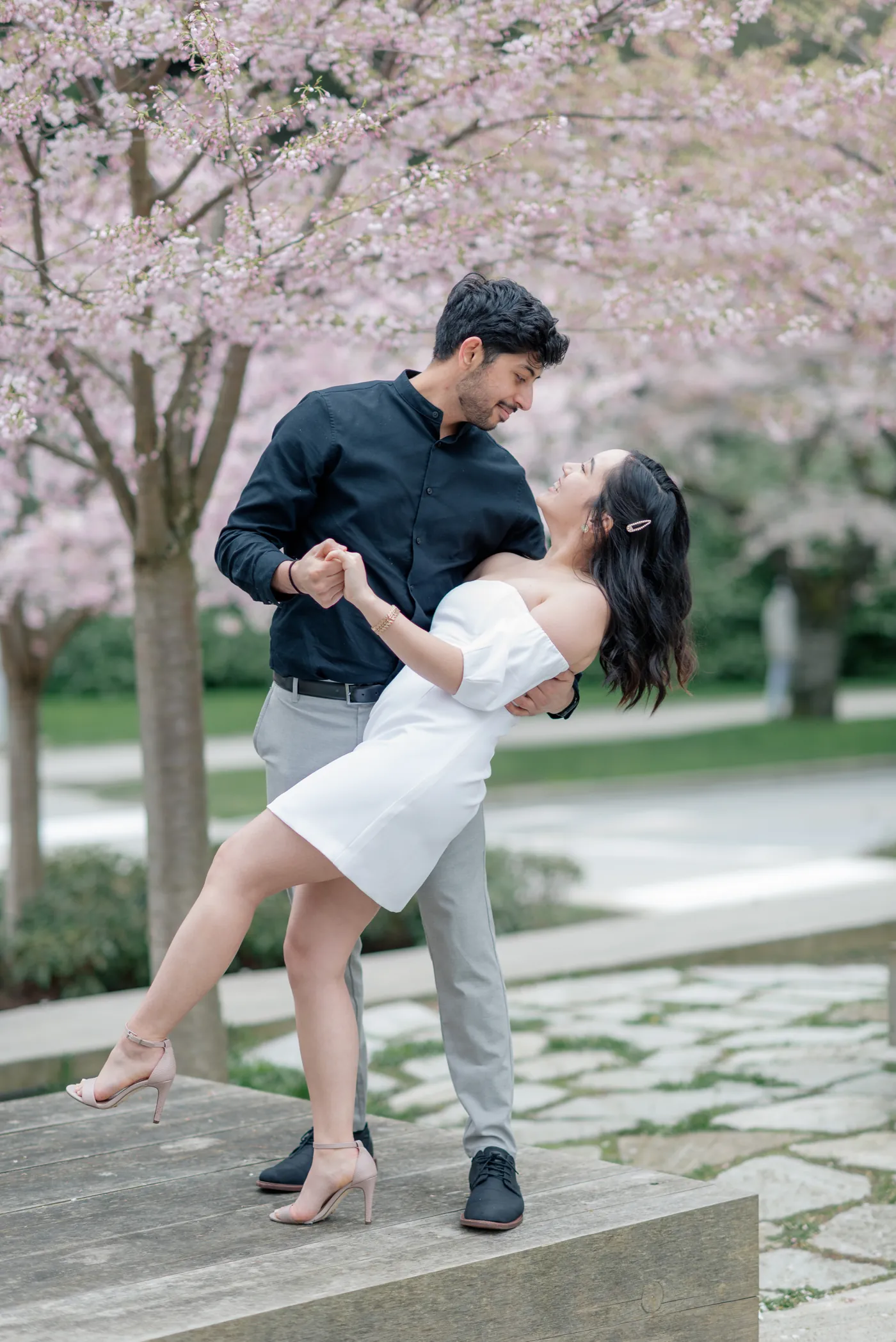 A romantic dip under the cherry blossoms. The man holds his partner as she leans back, both lost in each other’s gaze, surrounded by soft pink petals.