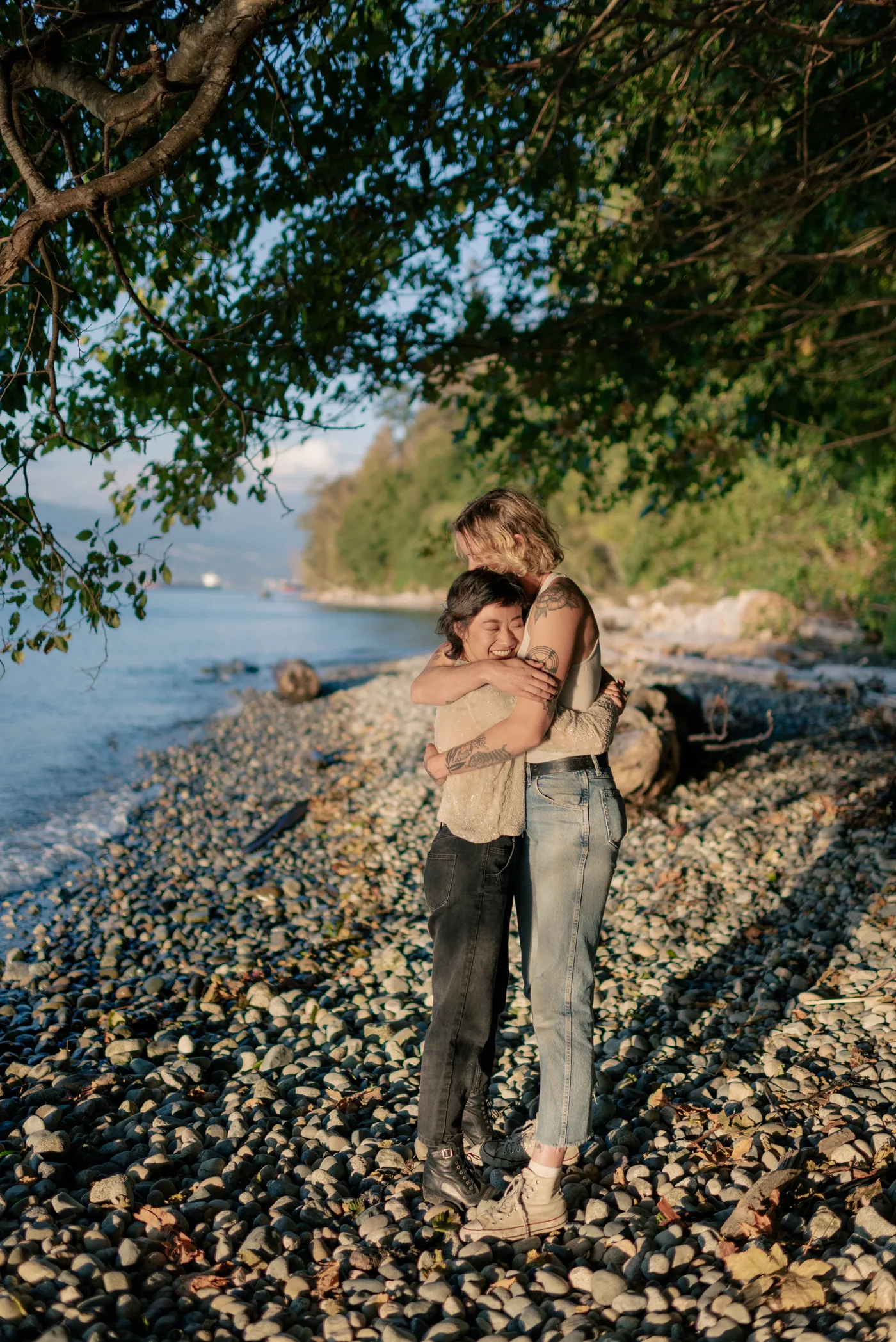 Newly engaged queer couple walking along the shore, celebrating their love. A dreamy and intimate engagement session on a scenic Canadian beach.
