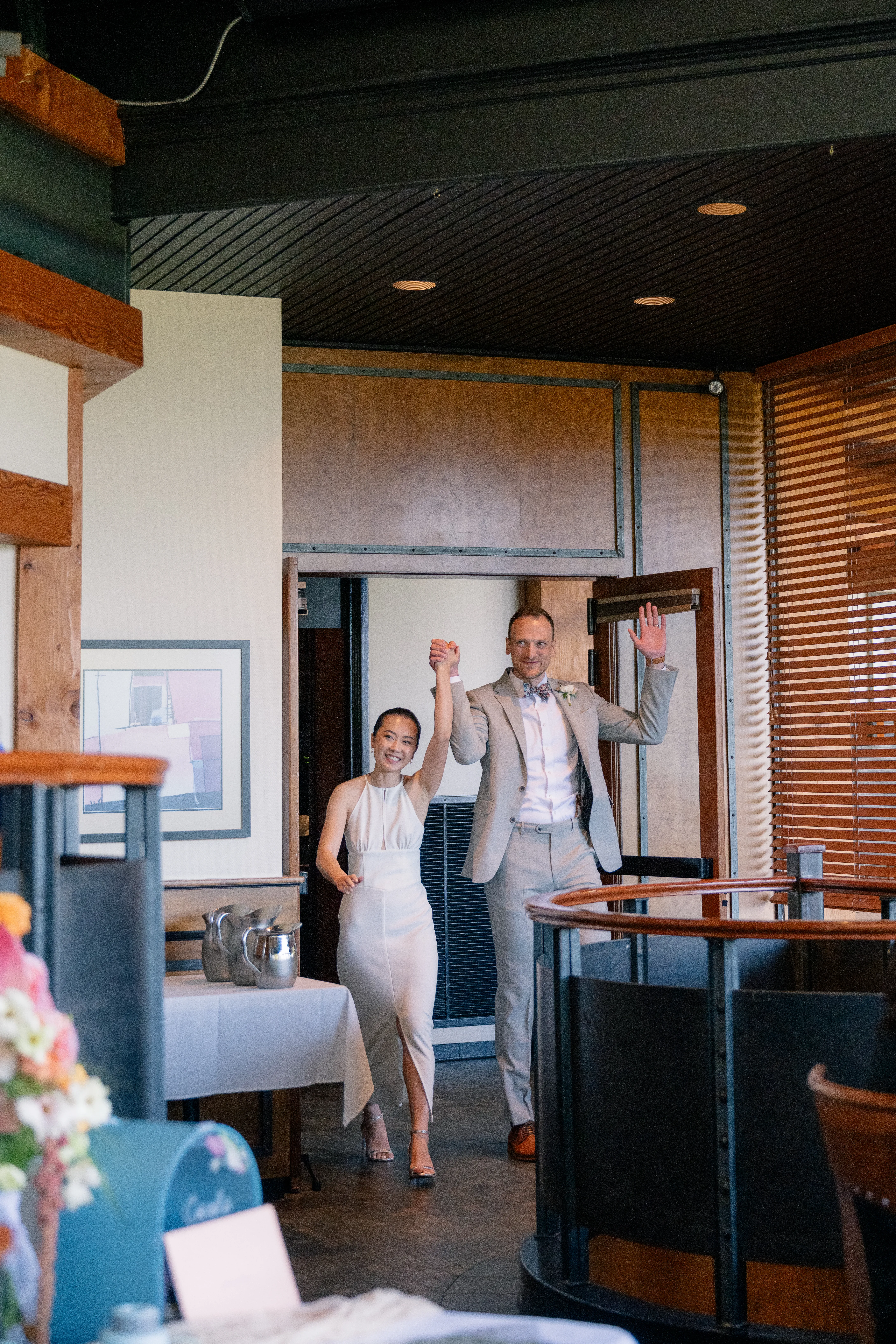 Bride and groom entering the reception venue, smiling and waving as guests cheer them on.