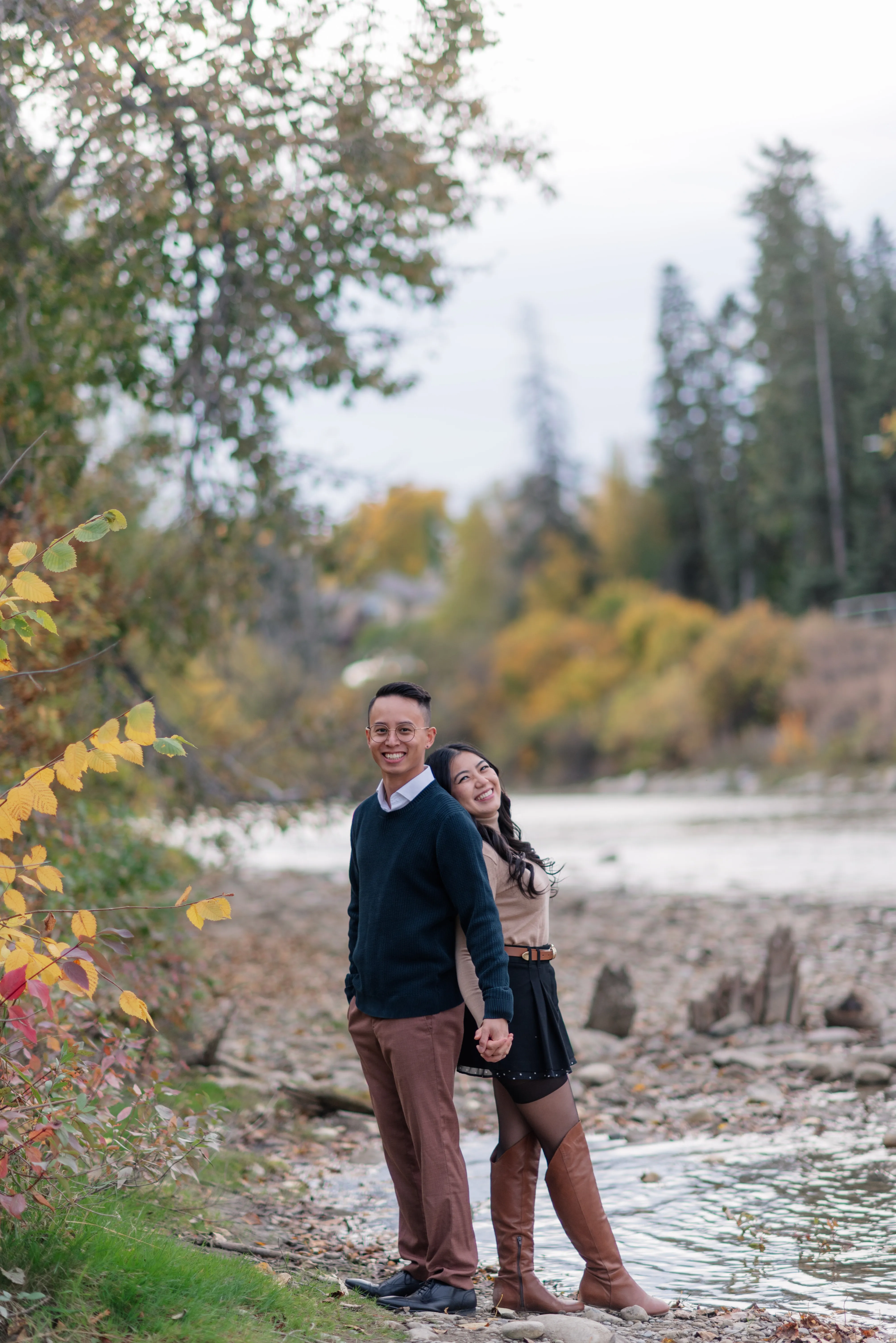 Engagement photo of couple standing on rocks along Elbow River in Calgary