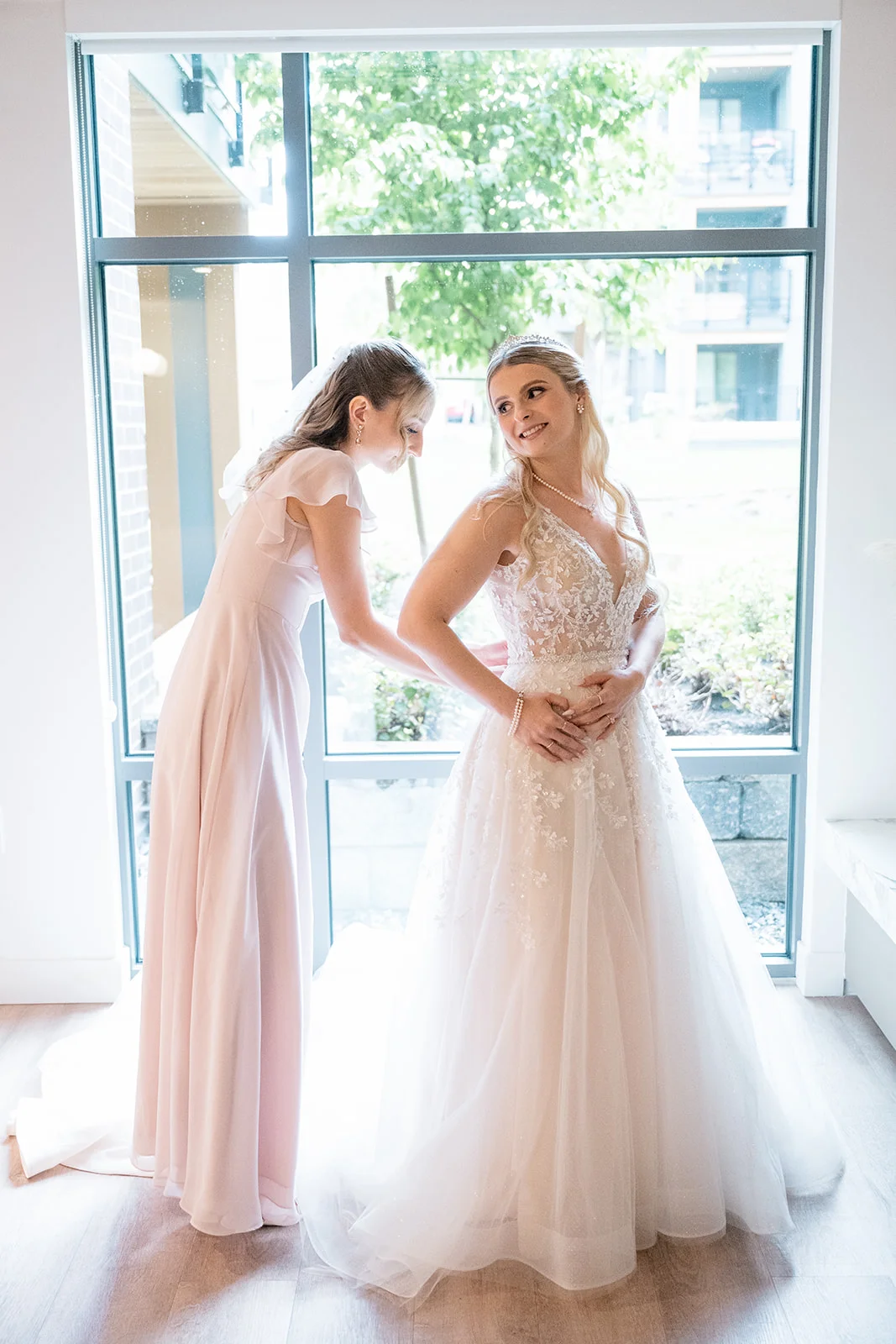 Bride getting ready, surrounded by her bridesmaids, while they help her into her lace wedding dress.