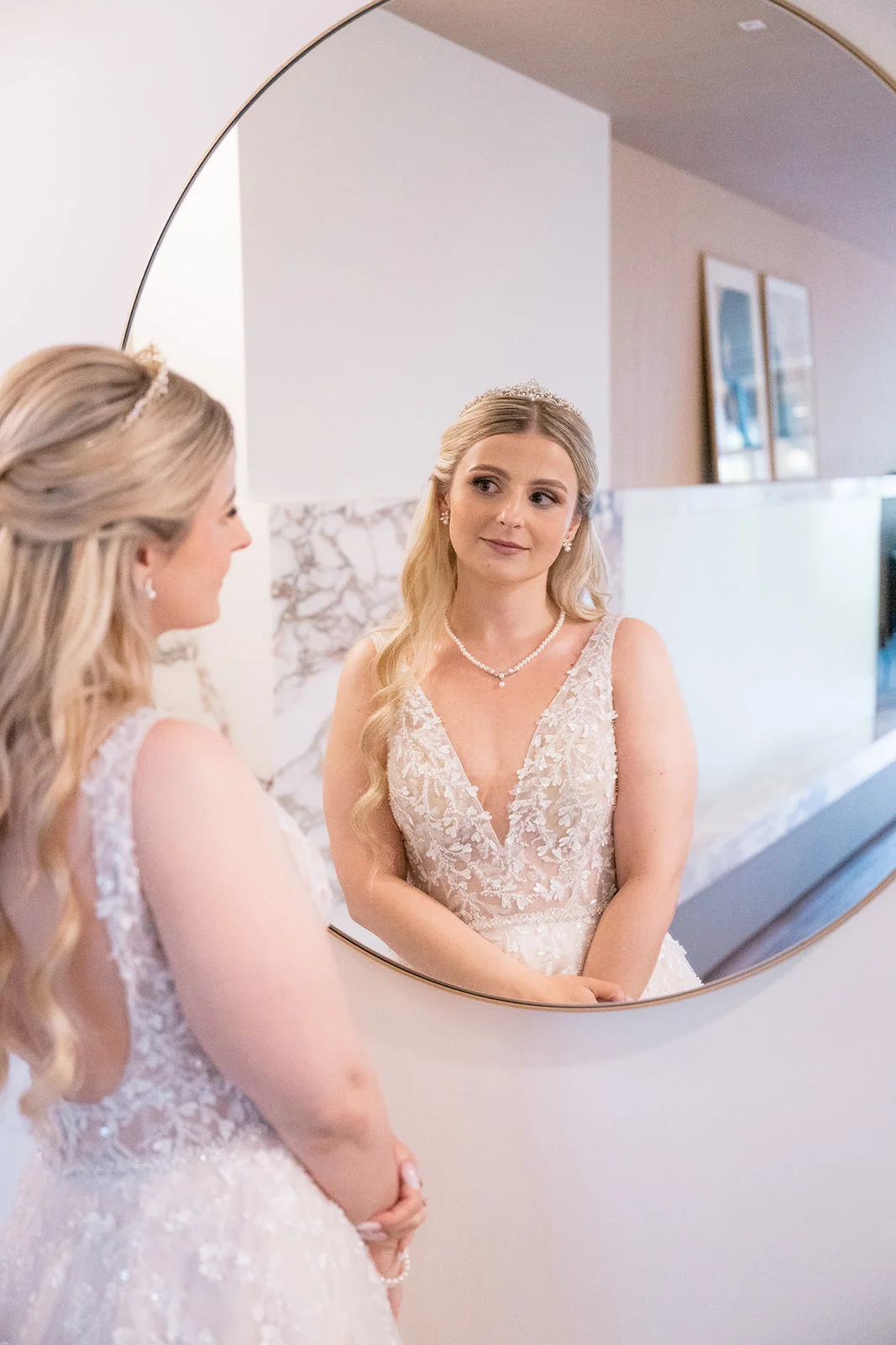 Bride getting ready, surrounded by her bridesmaids, while they help her into her lace wedding dress.