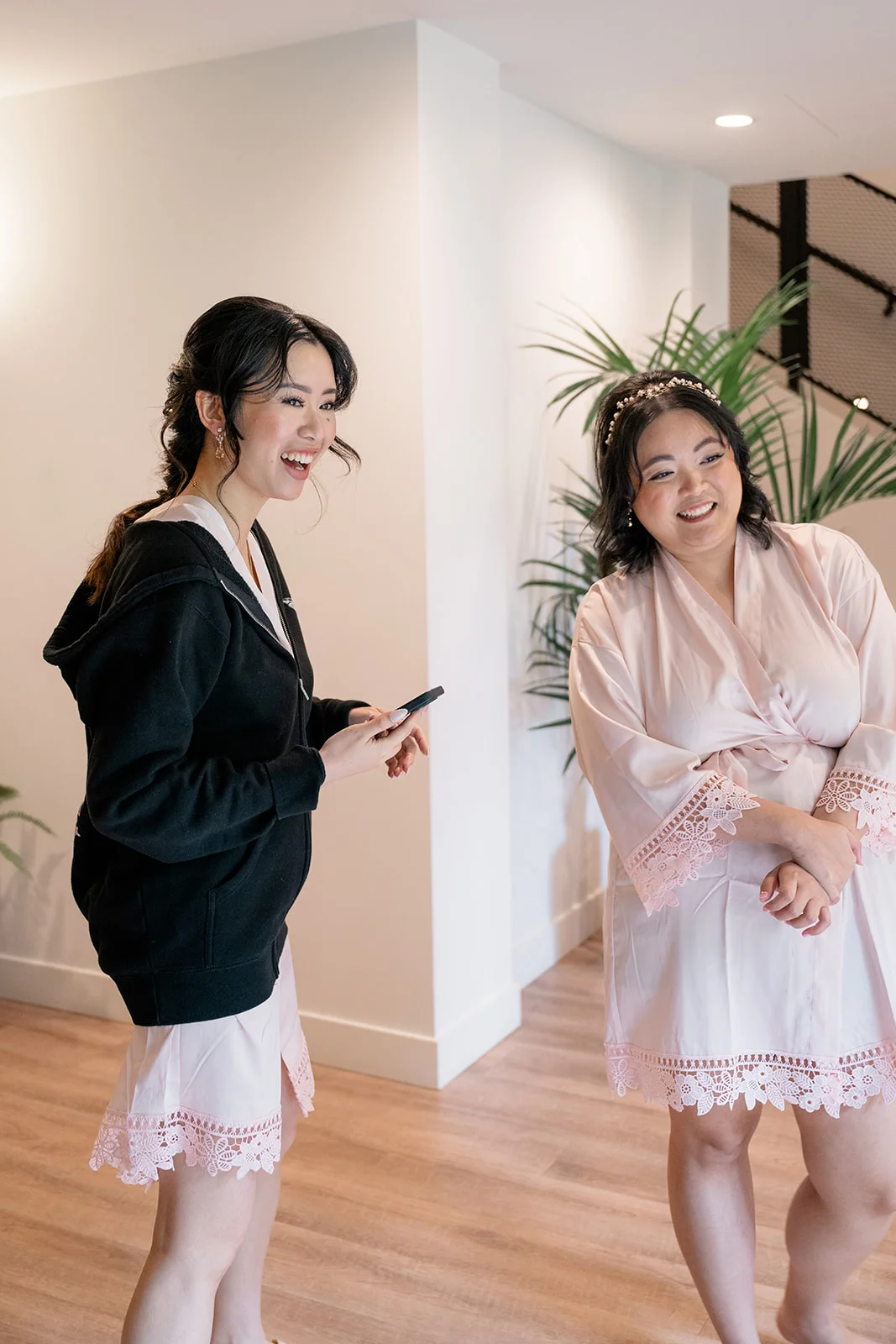 Bride getting ready, surrounded by her bridesmaids, while they help her into her lace wedding dress.
