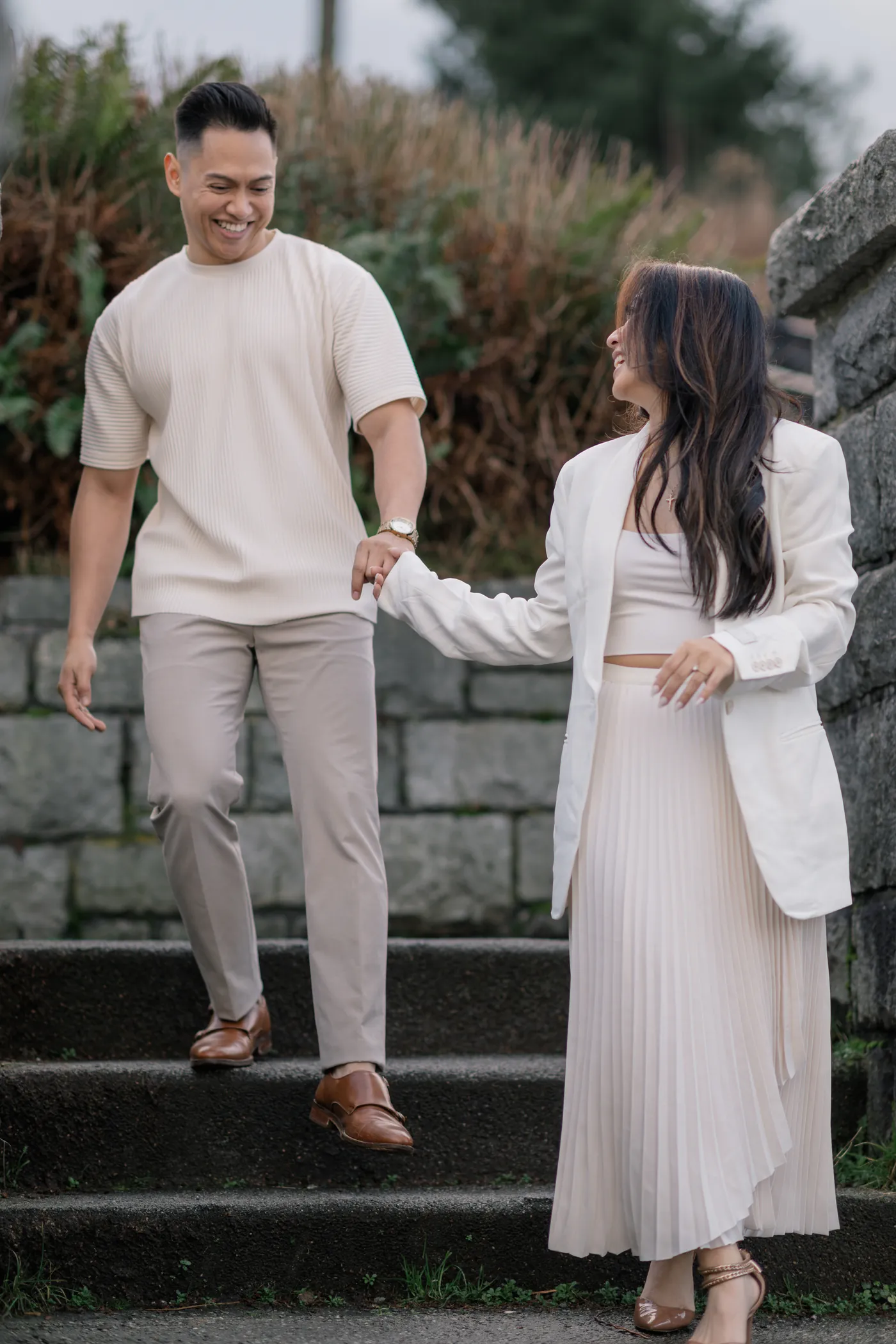 A couple walks down a stone staircase, hand in hand, during their engagement session at Stanley Park.