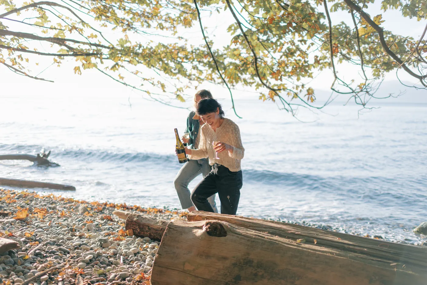 Newly engaged same-sex couple celebrating by the ocean with champagne. A candid and joyful moment during a post-proposal photography session on the Canadian coast.