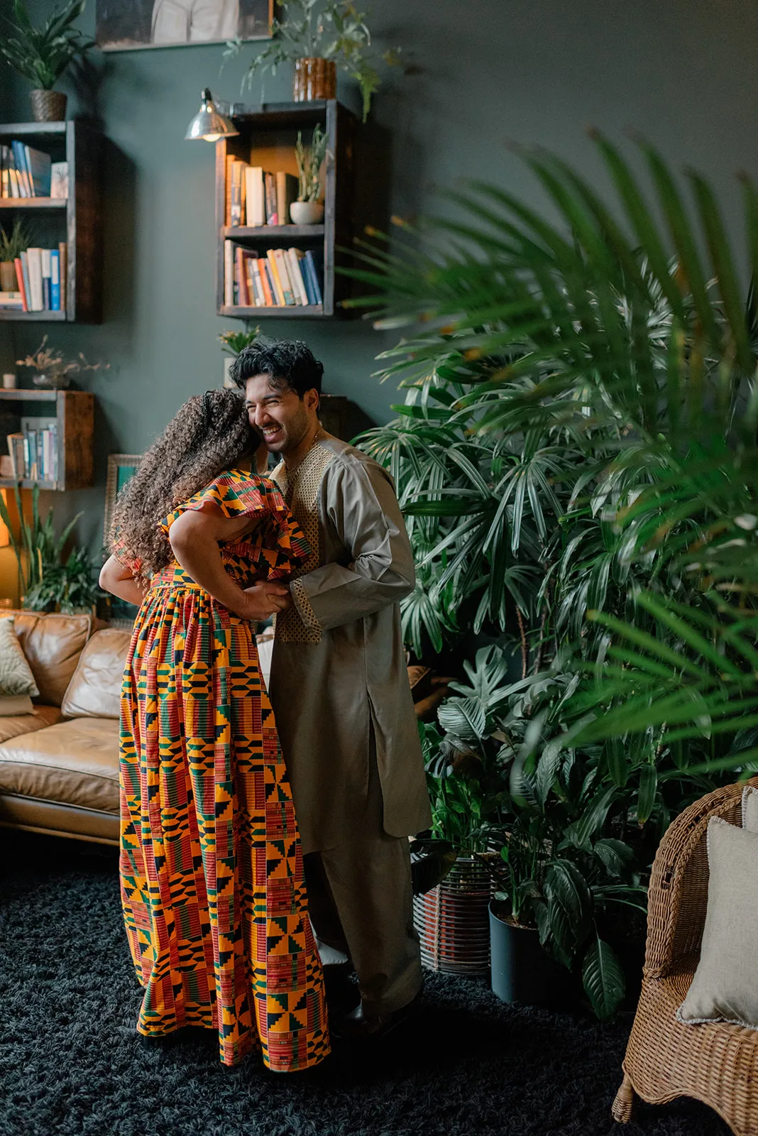C&J posing in vibrant cultural outfits during their engagement session at Loft Garden Oasis, with a backdrop of plants and natural light