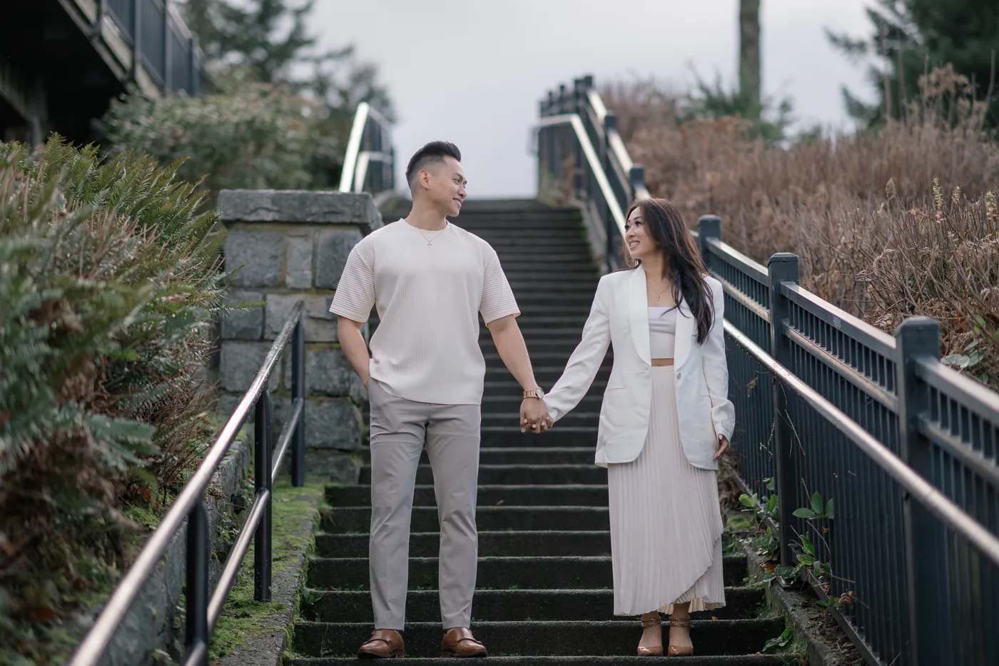 A couple stands hand in hand at the top of a staircase, gazing at each other lovingly during their Vancouver engagement session