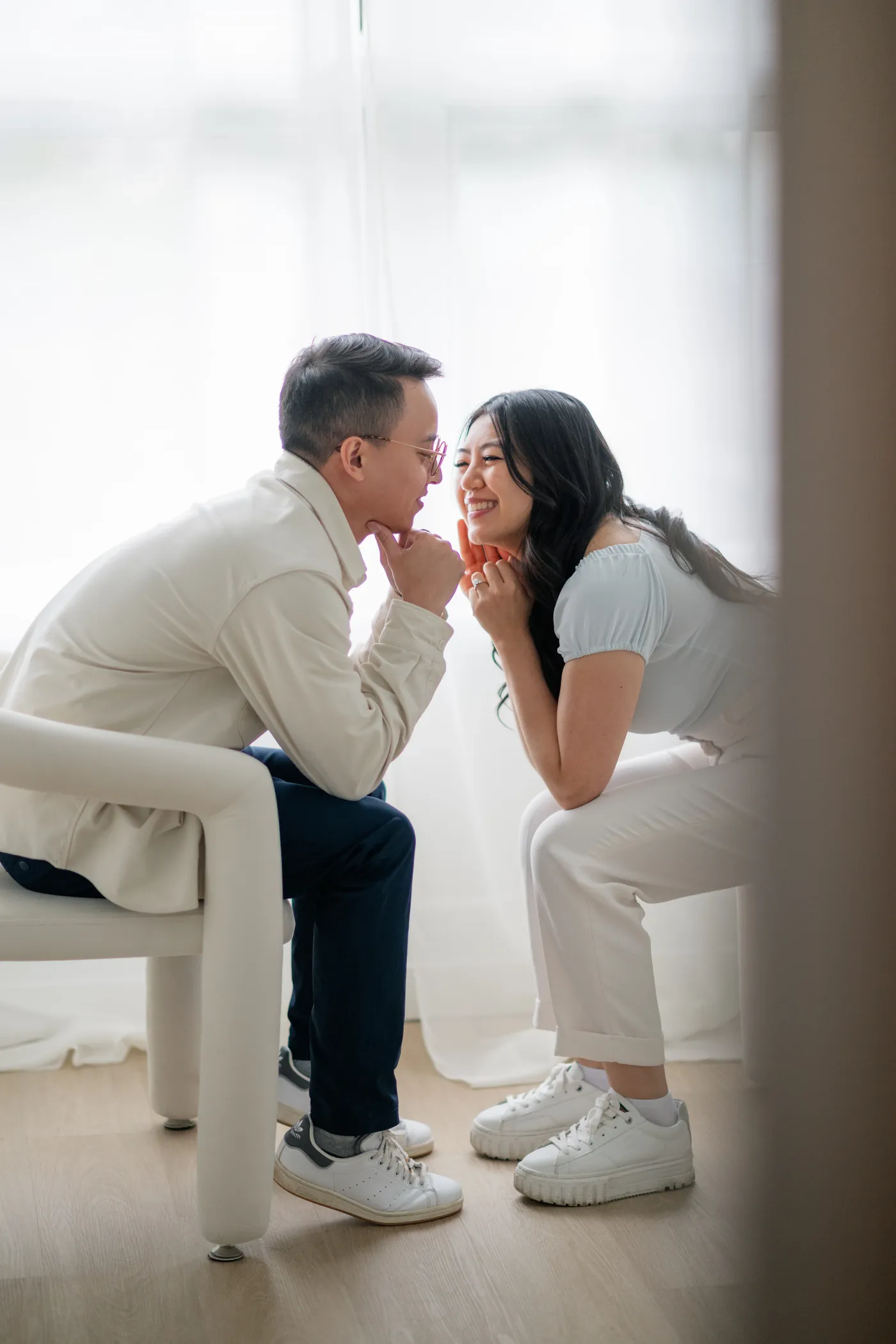 Close-up of engaged couple holding hands with soft natural light streaming in through large studio windows.