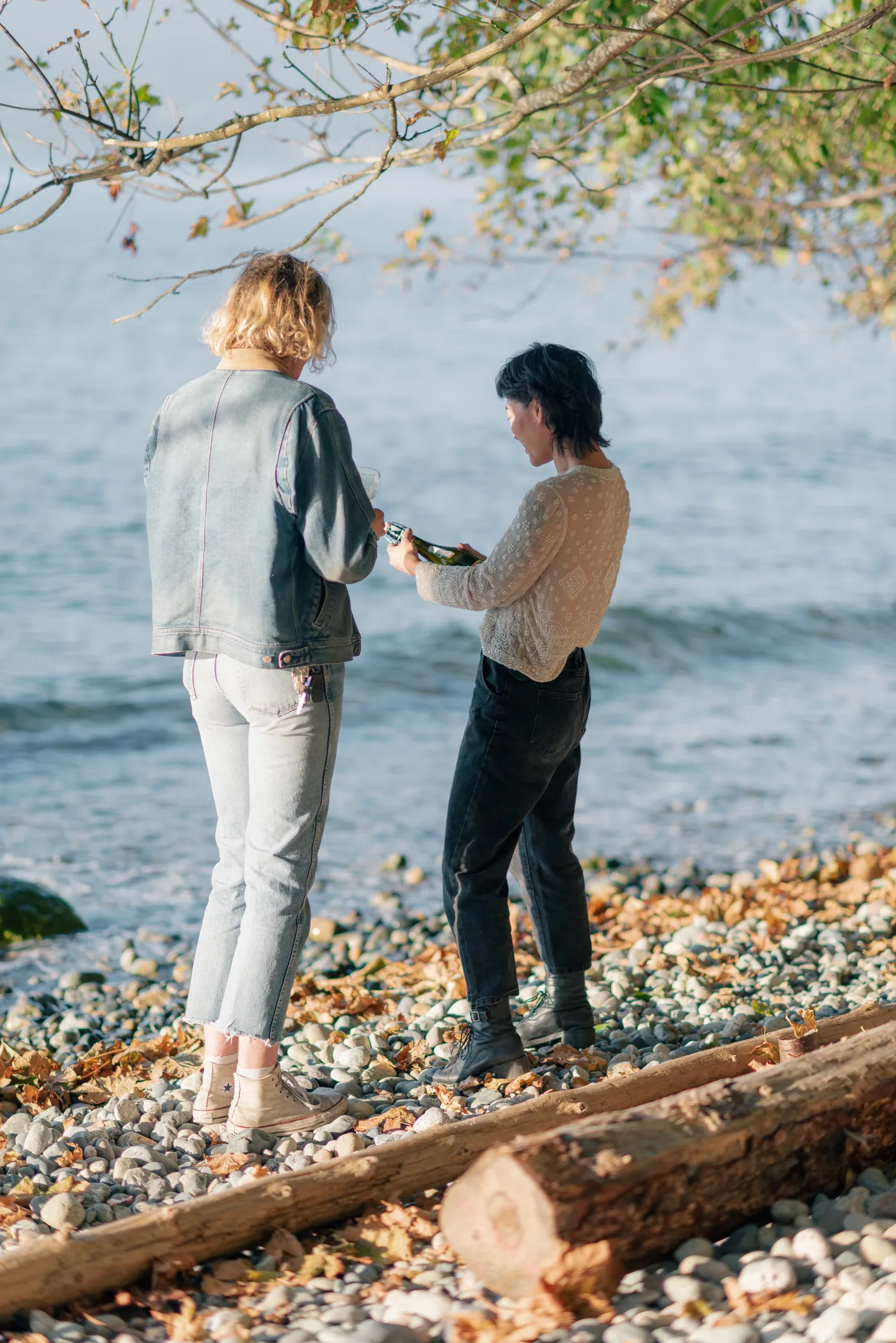 Newly engaged same-sex couple celebrating by the ocean with champagne. A candid and joyful moment during a post-proposal photography session on the Canadian coast.
