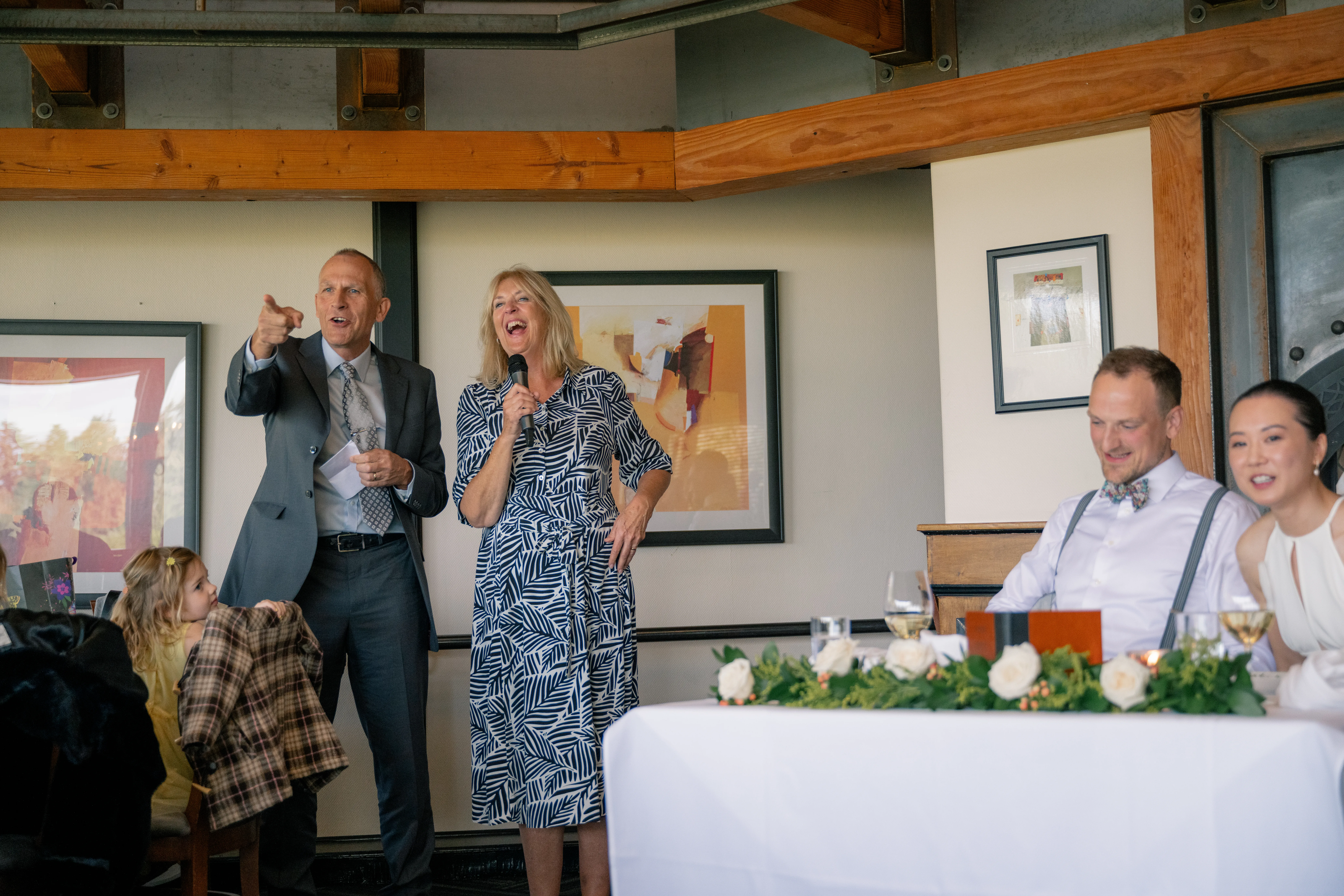 Family member standing and giving a speech at the wedding reception, while the bride and groom listen with smiles.