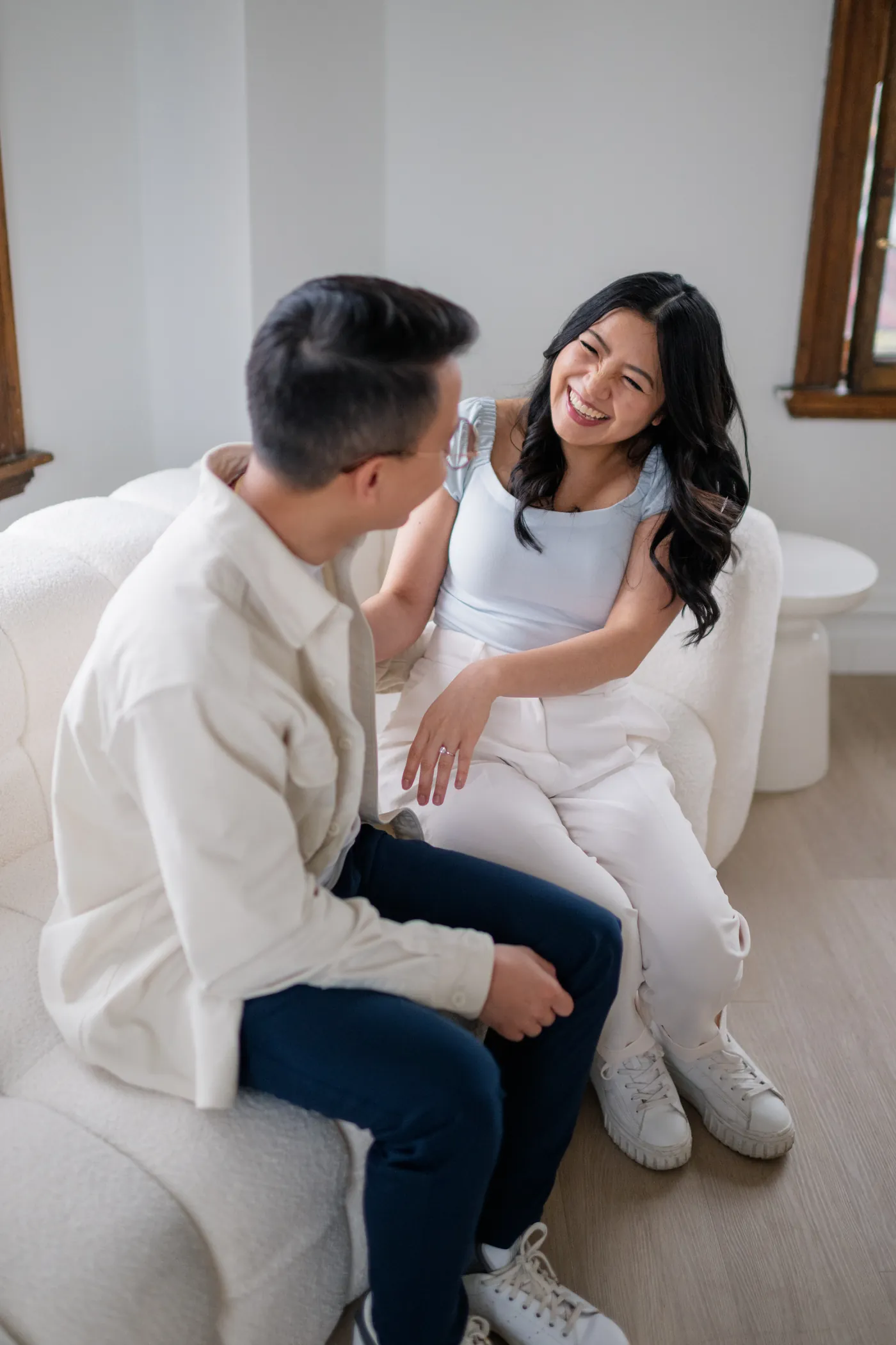 Engaged couple sitting close together, laughing and holding hands at a romantic indoor studio in Gastown.