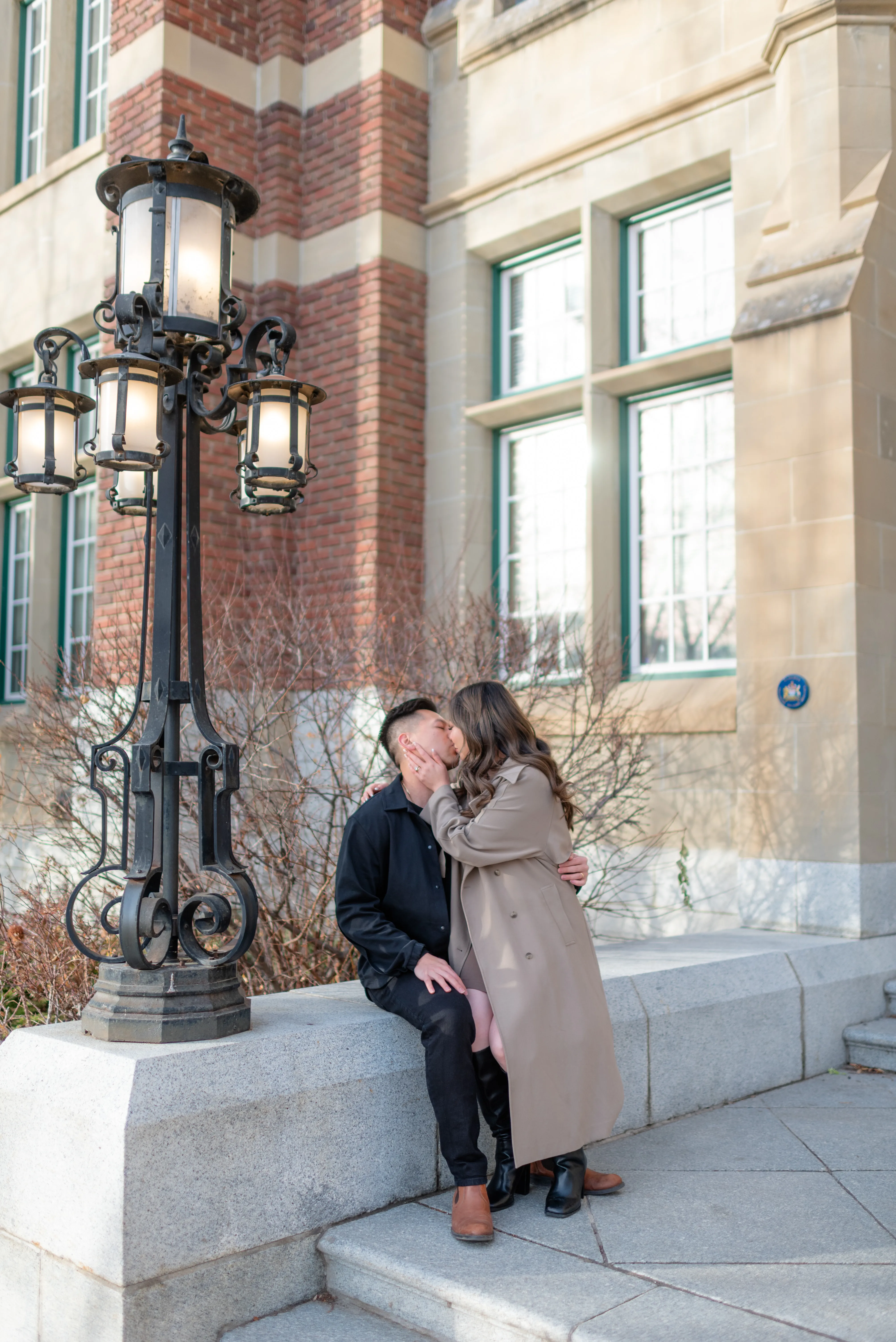 Candid engagement photo of a couple kissing against brick walls at Heritage Hall in Calgary