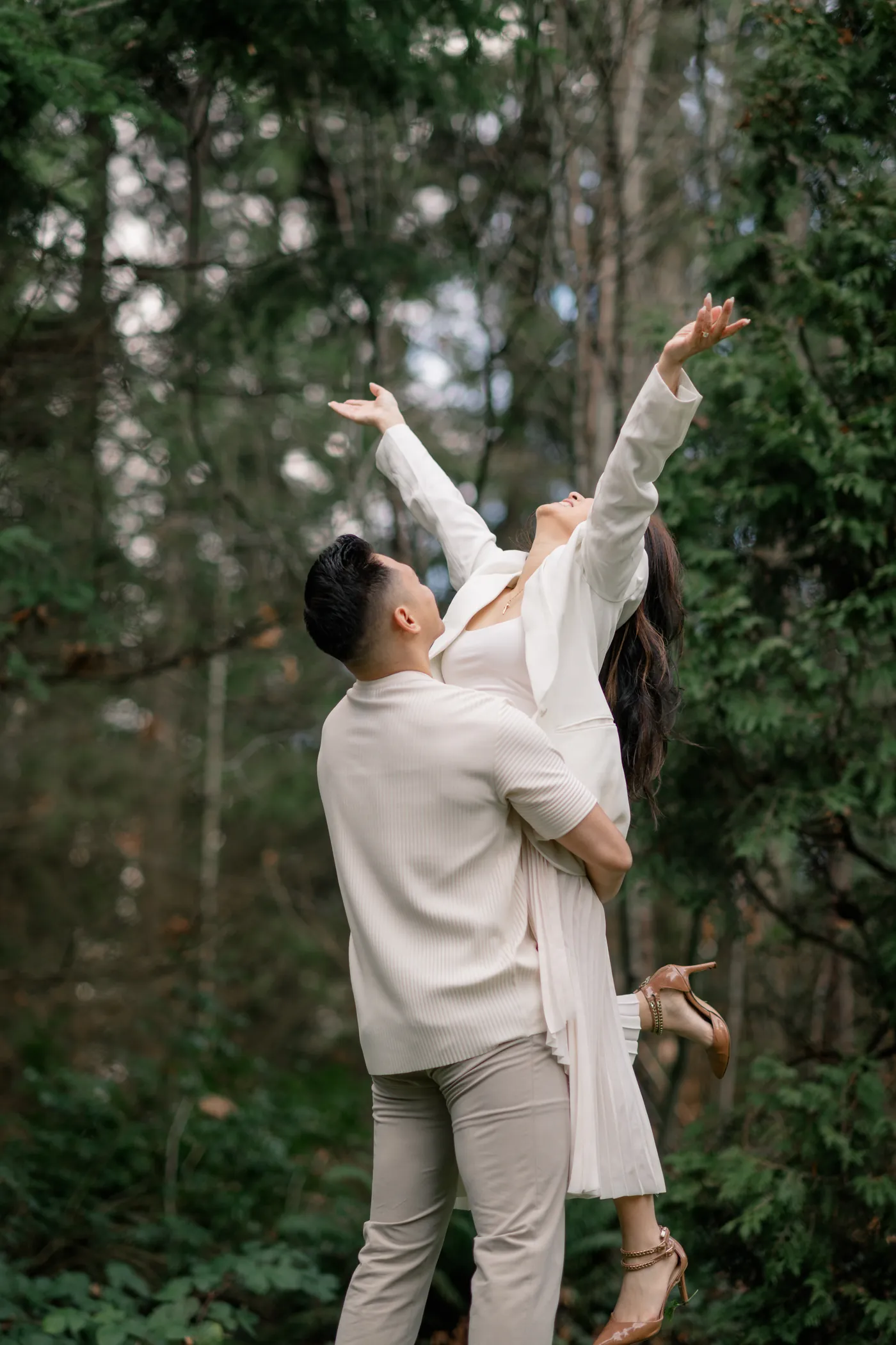 A joyful engagement moment where the groom-to-be lifts his fiancée into the air at Prospect Point in Stanley Park.