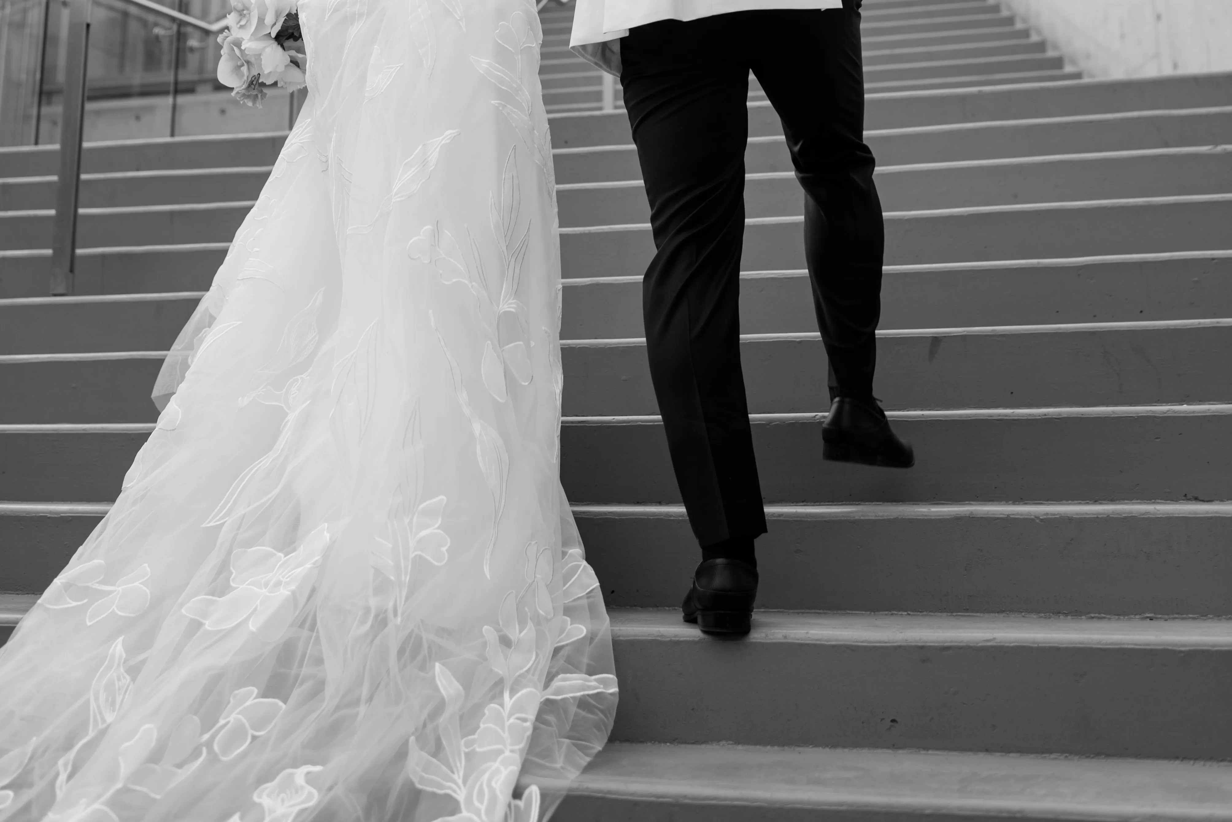 Close-up of wedding dress and groom’s shoes on concrete stairs in Calgary parkade