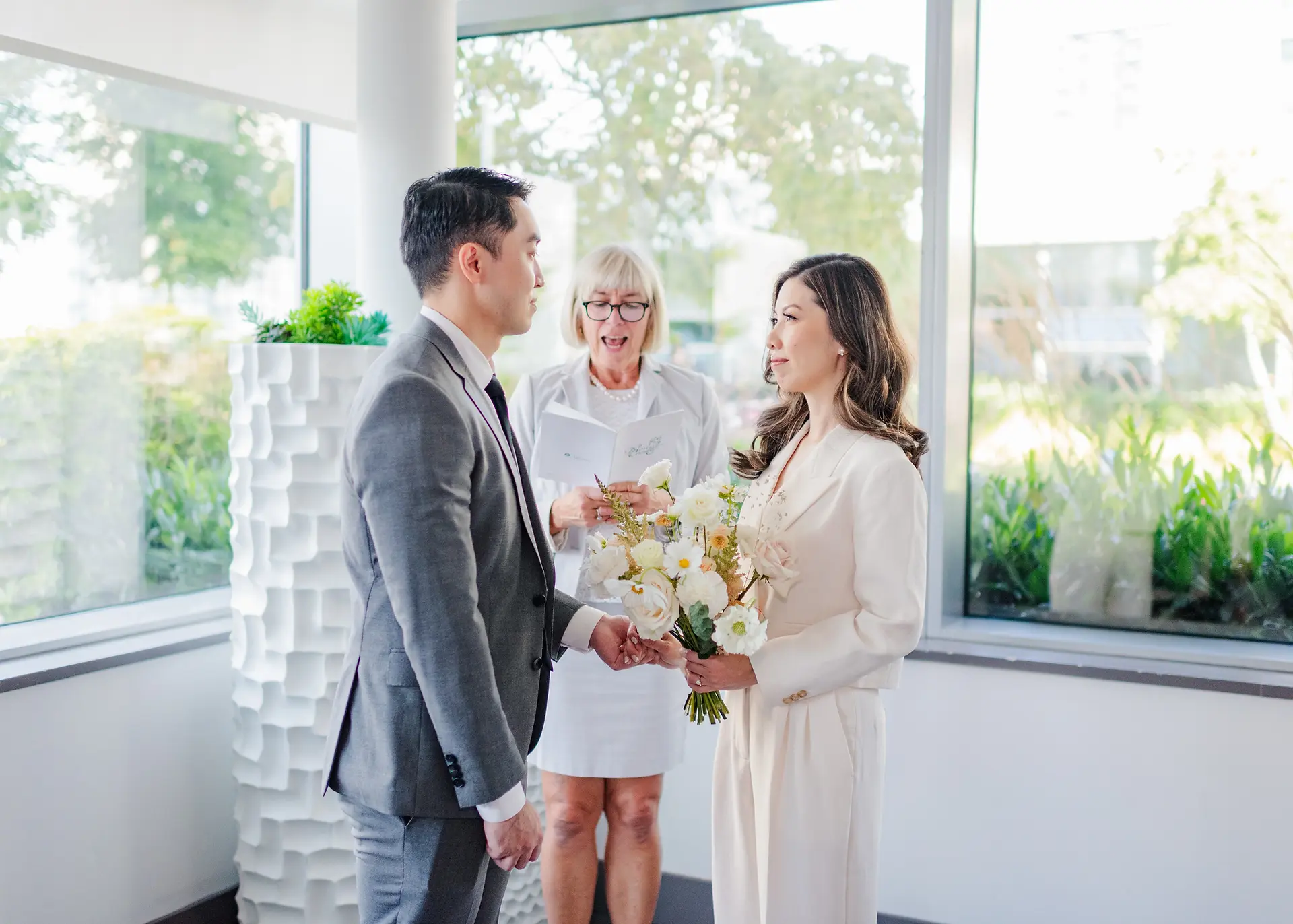 groom holding bride's hand during civil ceremony in amenities room in Burnaby, B.C.