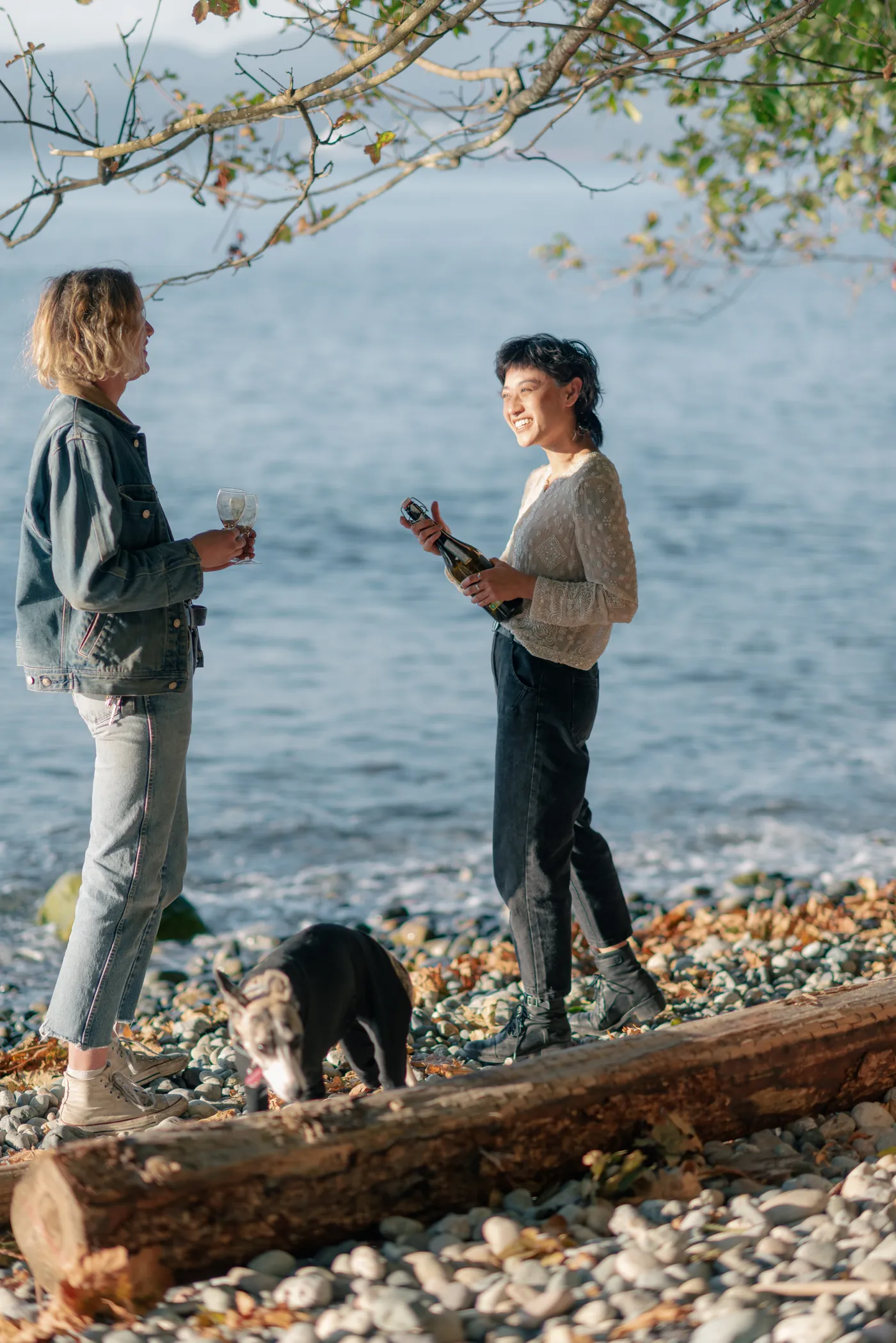 Newly engaged same-sex couple celebrating by the ocean with champagne. A candid and joyful moment during a post-proposal photography session on the Canadian coast.