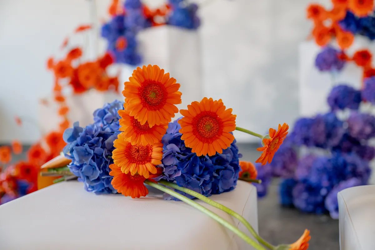 orange flowers and purple hydrangeas on modern white pedestals in a minimalist industrial venue, showcasing bold wedding decor.