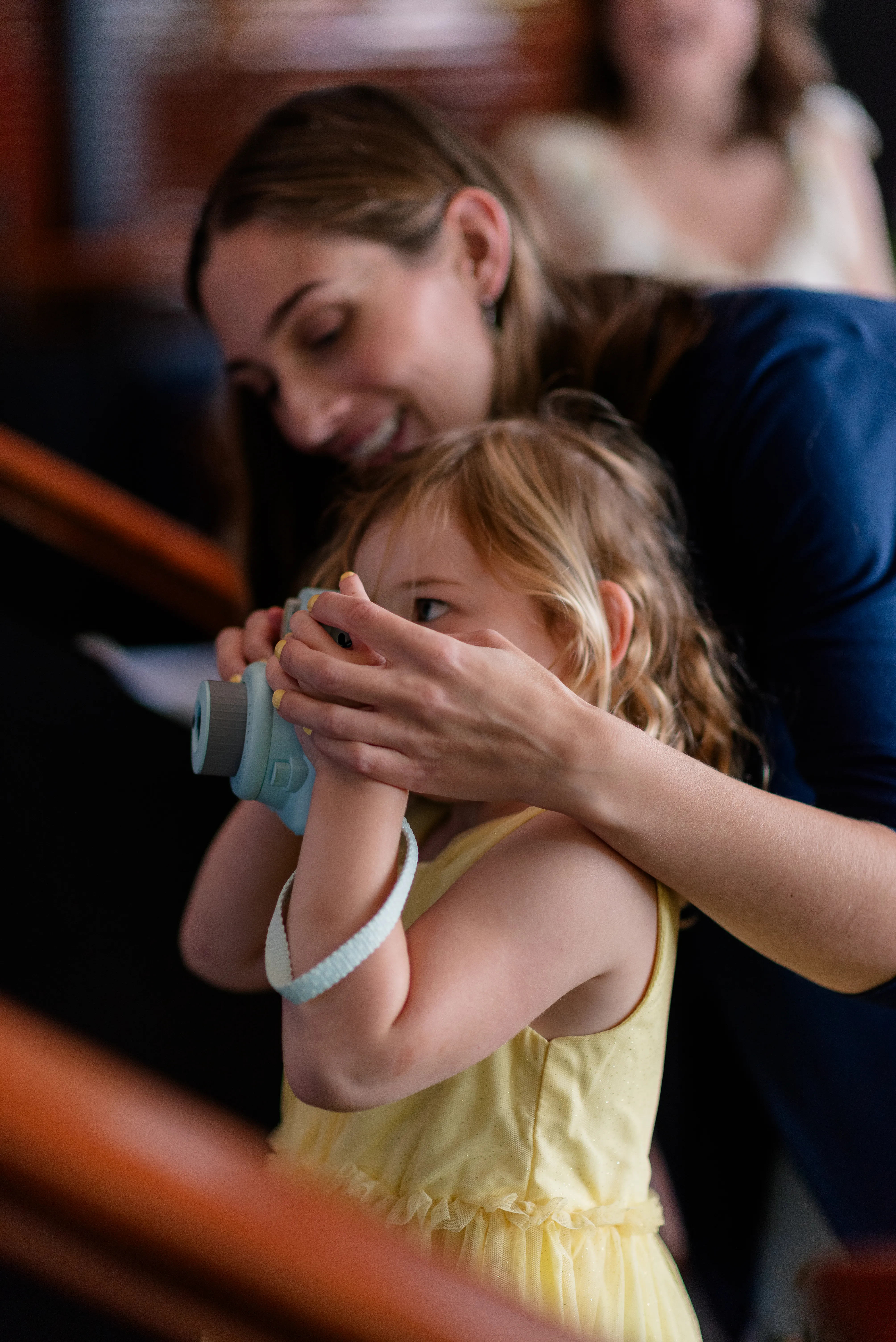 Little girl holding a toy camera, being helped by an adult to take a photo at the wedding reception