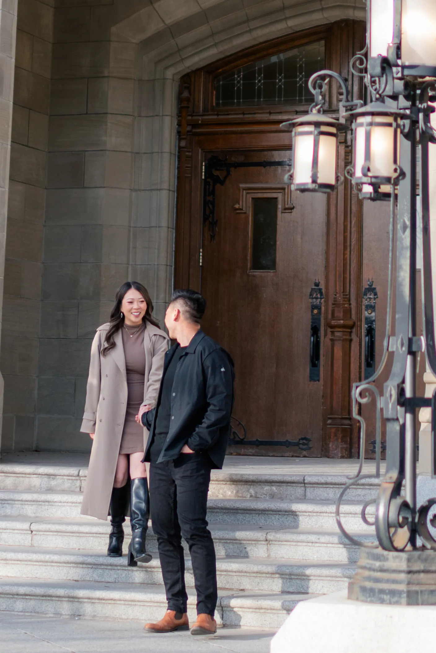 Engaged couple walking down the stone steps beneath the arched entrance of Heritage Hall in Calgary