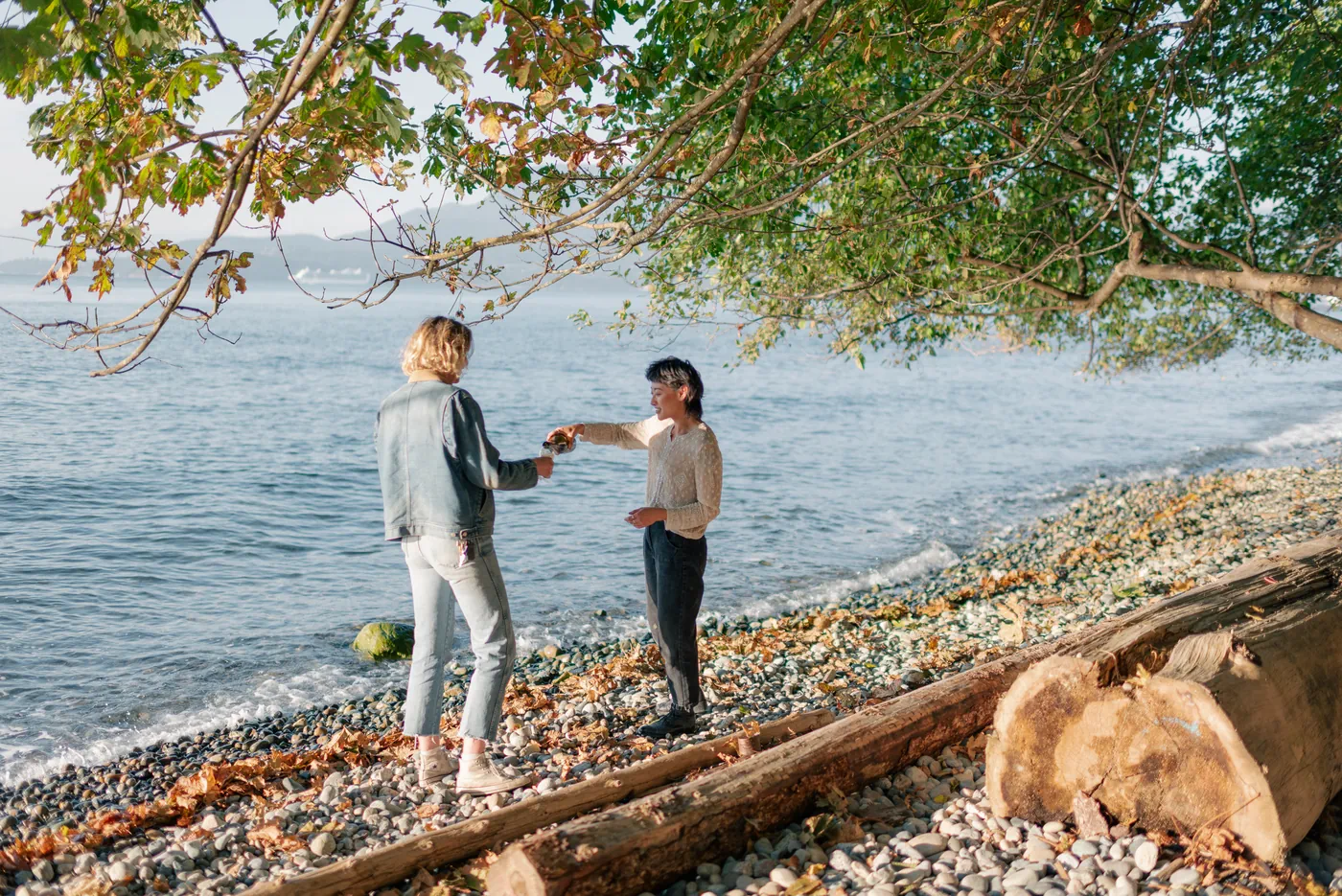 Newly engaged same-sex couple celebrating by the ocean with champagne. A candid and joyful moment during a post-proposal photography session on the Canadian coast.