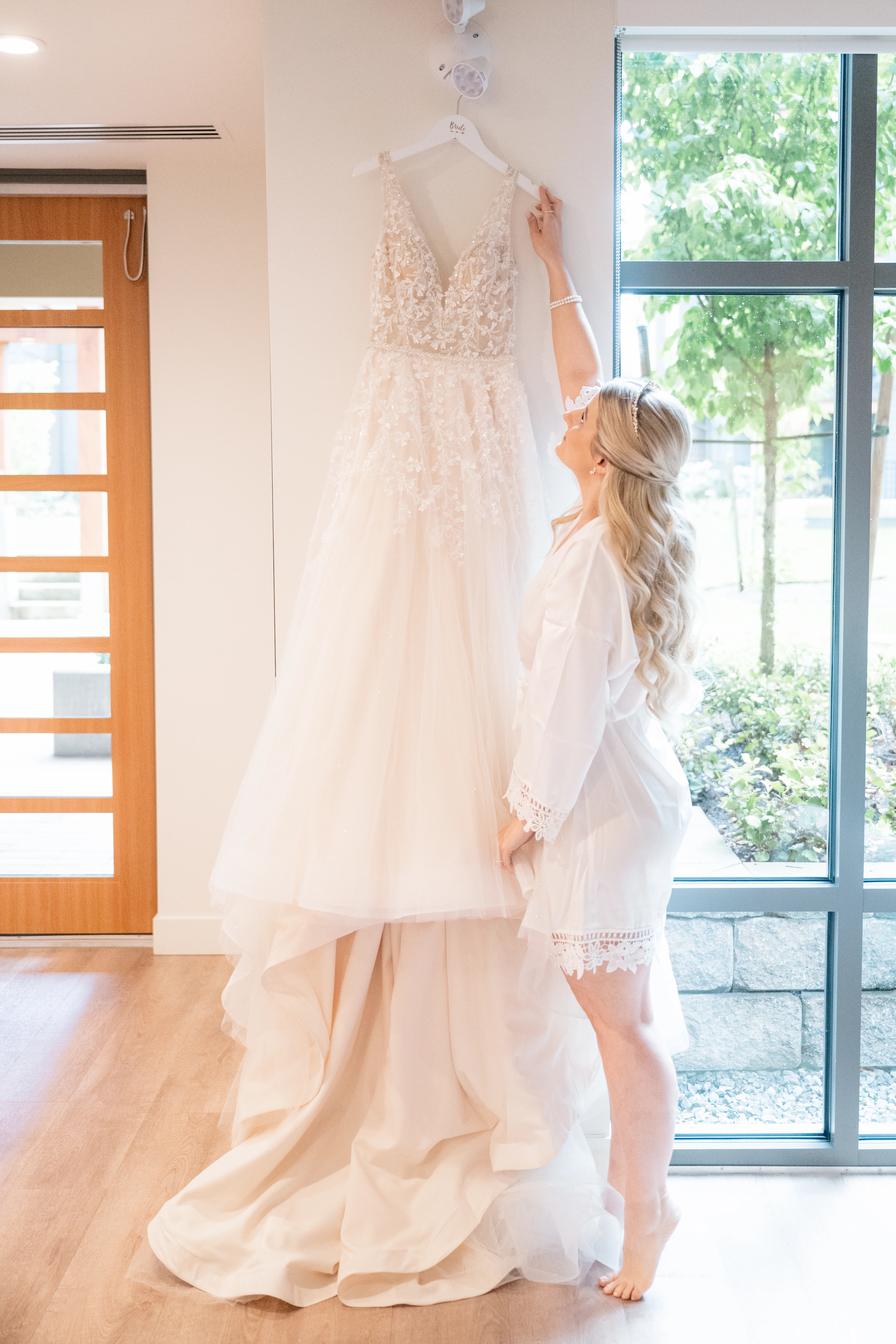 Bride getting ready, surrounded by her bridesmaids, while they help her into her lace wedding dress.