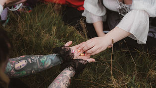 A tattoed fae receiving small resin babies from a burly wench