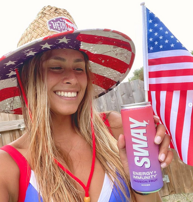Girl with a straw hat drinking a Sway Energy drink in front of American flag