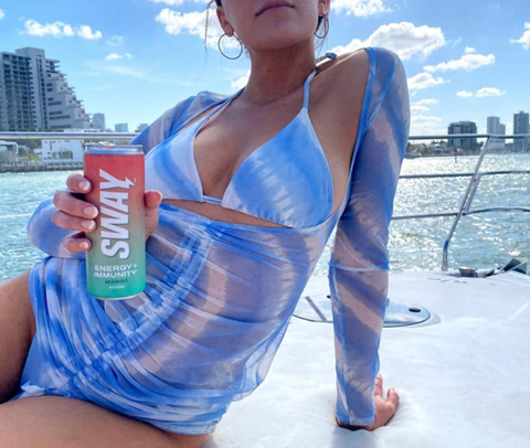 female on a beach holding a Sway Energy Drink Mango
