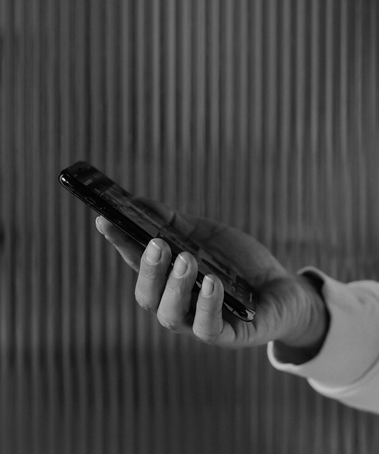 Hand holding phone, black and white photo. Background is textured lines, rubysignorelli.com.