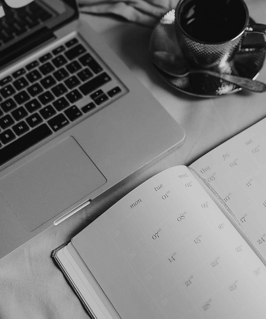 Laptop displays 5:20 on bed beside coffee and open notebook