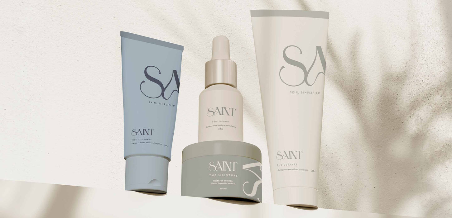 SAINT skincare full product range including cleanse tubes serum and moisture jar on textured white surface — luxury skincare brand identity and packaging design by Studio Ruby Signorelli