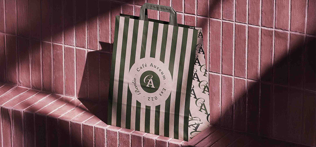 Café Aureum striped paper shopping bag with embossed monogram seal, styled on sunlit tile — hospitality packaging design by Studio Ruby Signorelli, California.